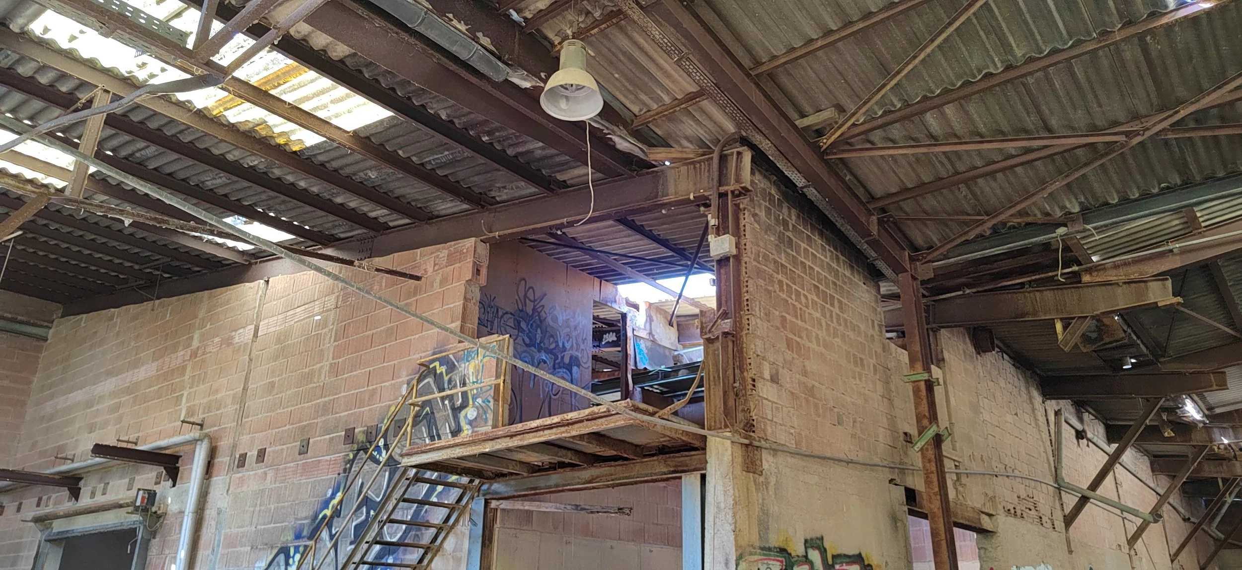 Innenansicht eines alten, abbruchreifen Gebäudes mit Baugerüst, graffiti an den Wänden, unvollständigem Dach und offenen Fenstern.