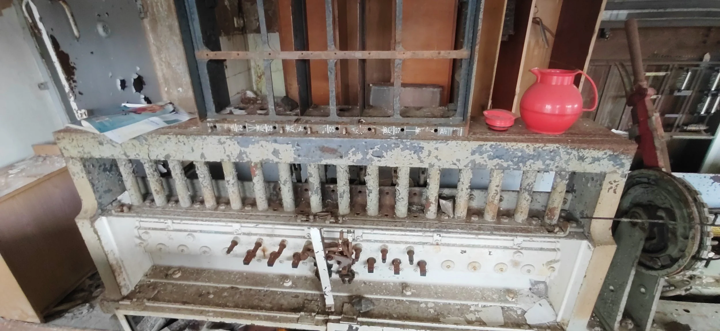 Alter, verrosteter Maschinenrahmen in einer Werkstatt mit roter Keramikkanne und kleinen Schalen auf einem rustikalen Tisch.