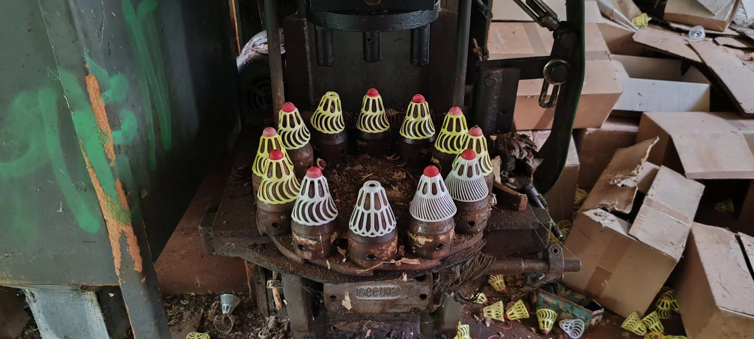 Mehrere weiße und gelbe Gitterhütten für Schnecken, die auf einer alten Maschine sitzen, in einem Werkzeugraum mit Kartons im Hintergrund.