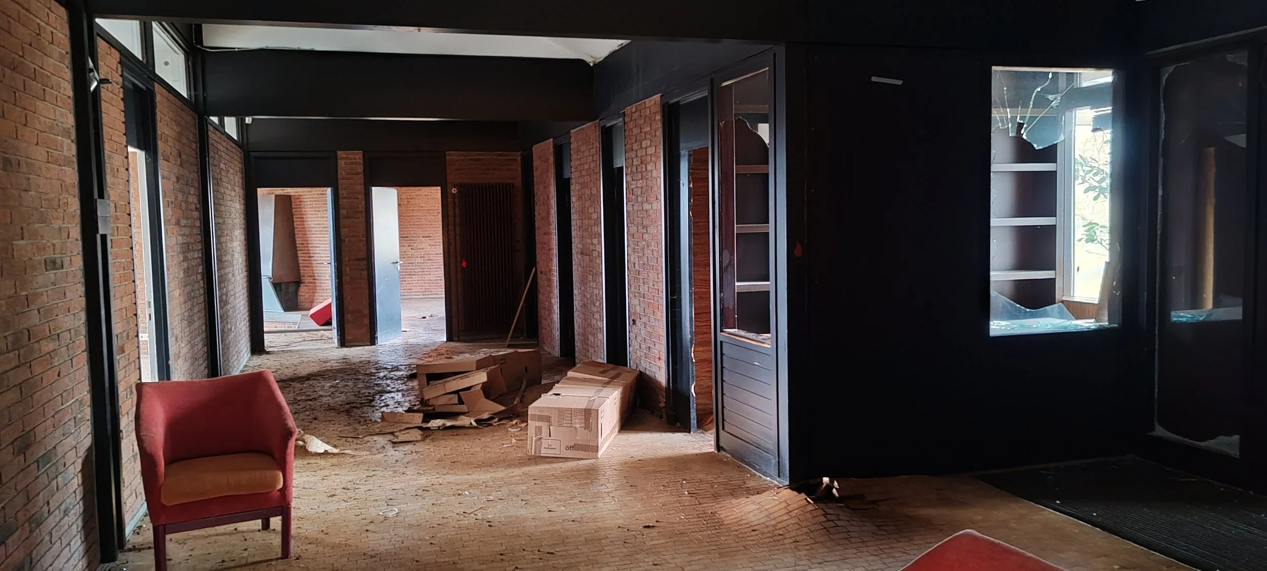 Innenraum eines Gebäudes im Umbau oder Renovierung mit Ziegelwänden, Staub, Verpackungskartons und einem roten Stuhl.