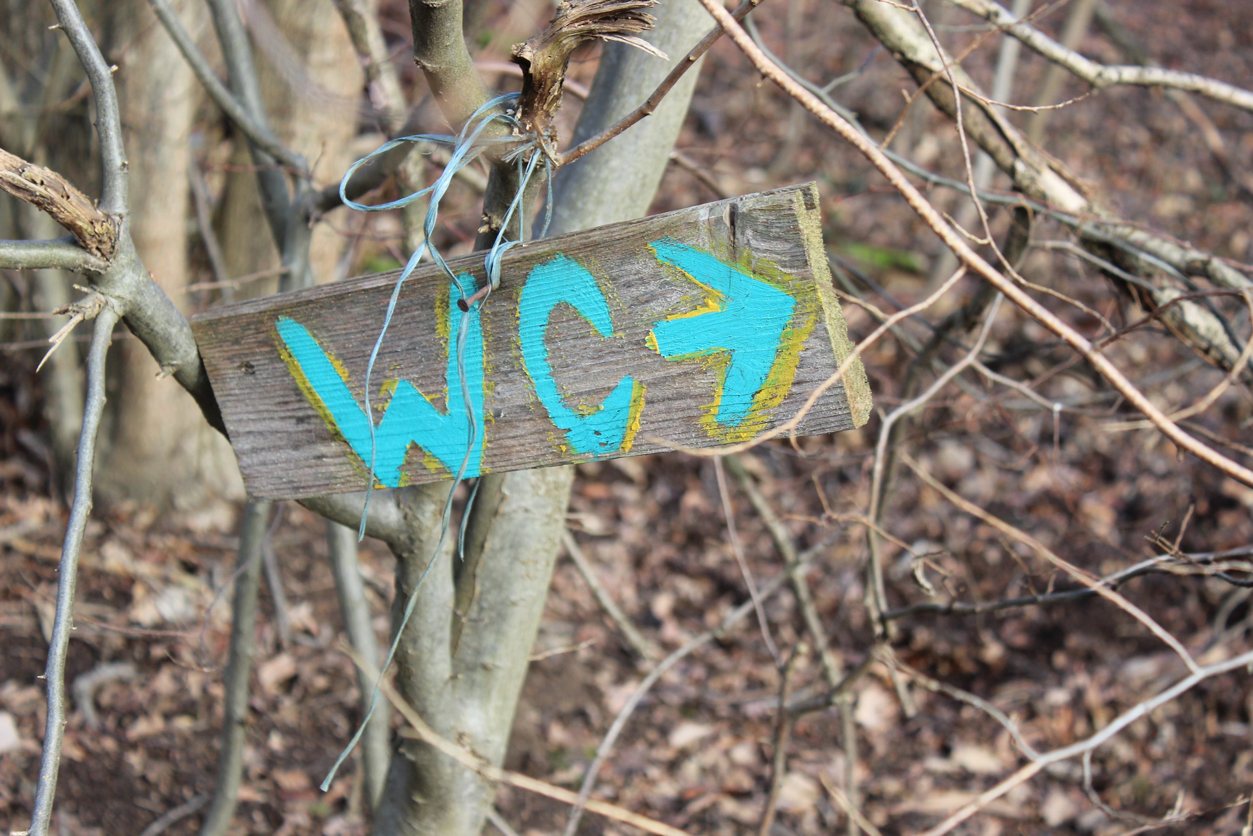 Ein Holzschild mit der Aufschrift 'WIC' und einem Pfeil, das an einem Baum in einem Wald befestigt ist.