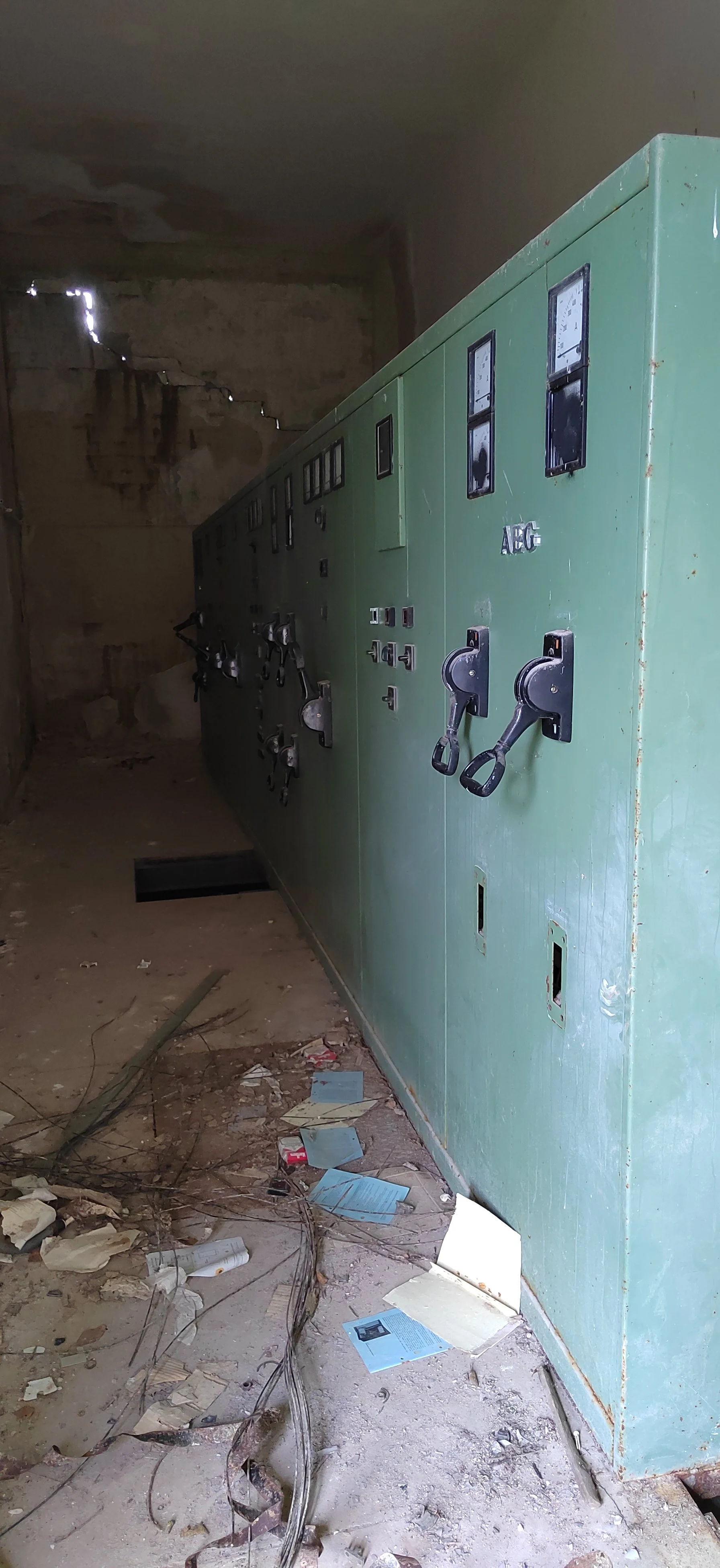 Alter, verlassener Raum mit einer grünen elektrischen Steuerungs- oder Verteilerbox, Staub, Schmutz, verstreute Papiere und Kabel auf dem Boden.