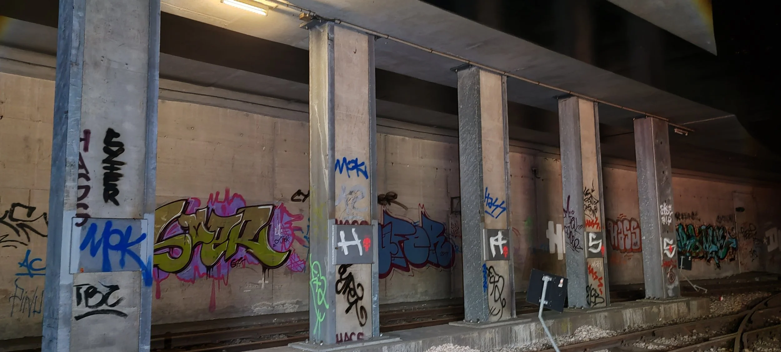Unterführung mit Betonstützen und Gleisen, bedeckt mit buntem Graffiti an den Wänden und Stützen.