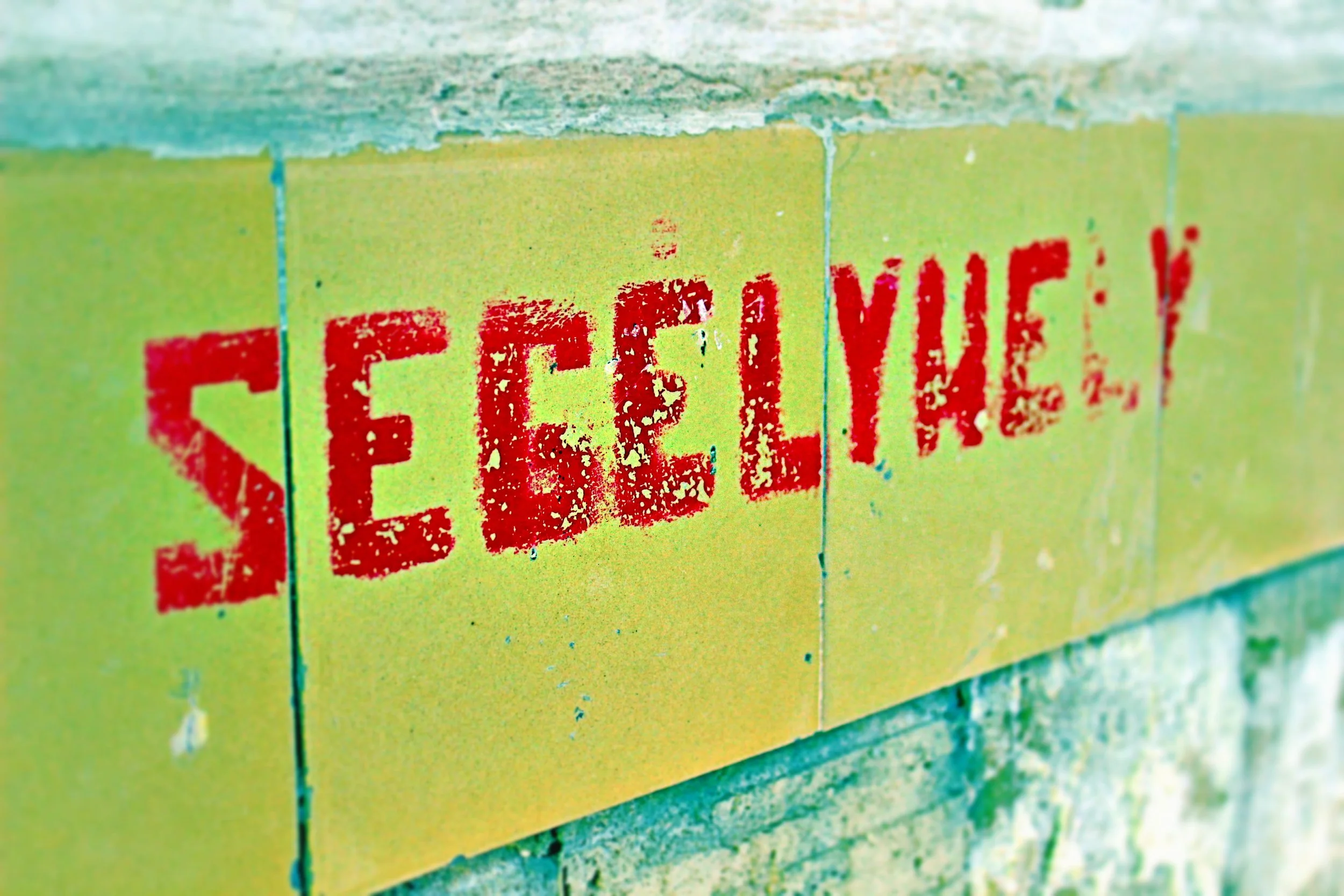 Hinweisschild mit roter Aufschrift 'SEGELN' auf gelbem Hintergrund, an einer Mauer angebracht.