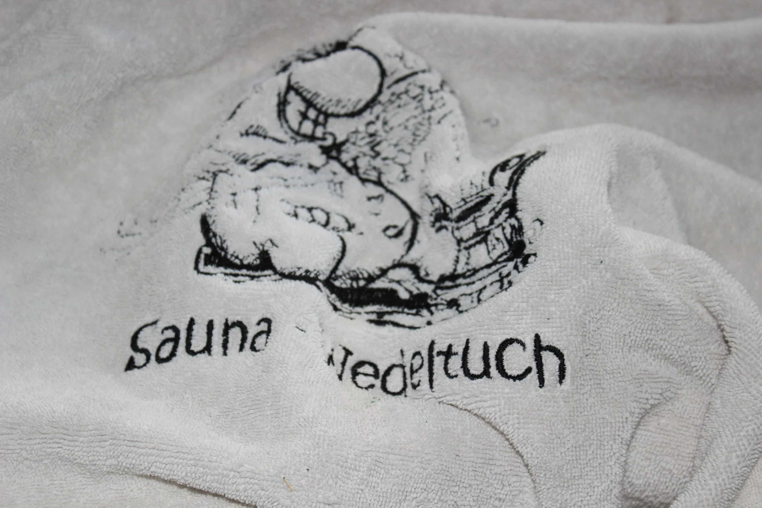 Weiße Handtuch mit schwarzem Comic-ähnlichem Druck eines lachenden Mannes, der eine Brille trägt, und den Worten "suna tretenuch".