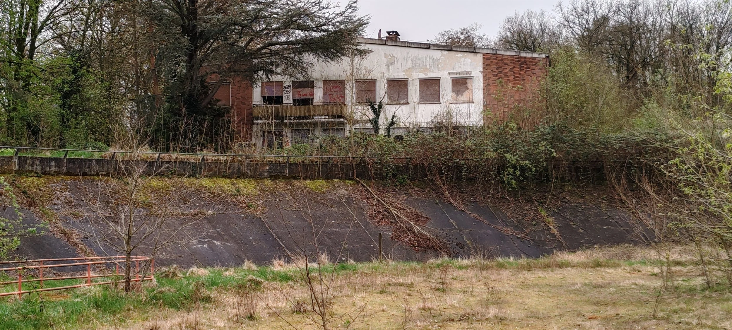 Verfallene, verlassene Villa auf einem Hügel, umgeben von Bäumen und verfallener Natur, mit Graffiti an den Fenstern und vorderer Wand.