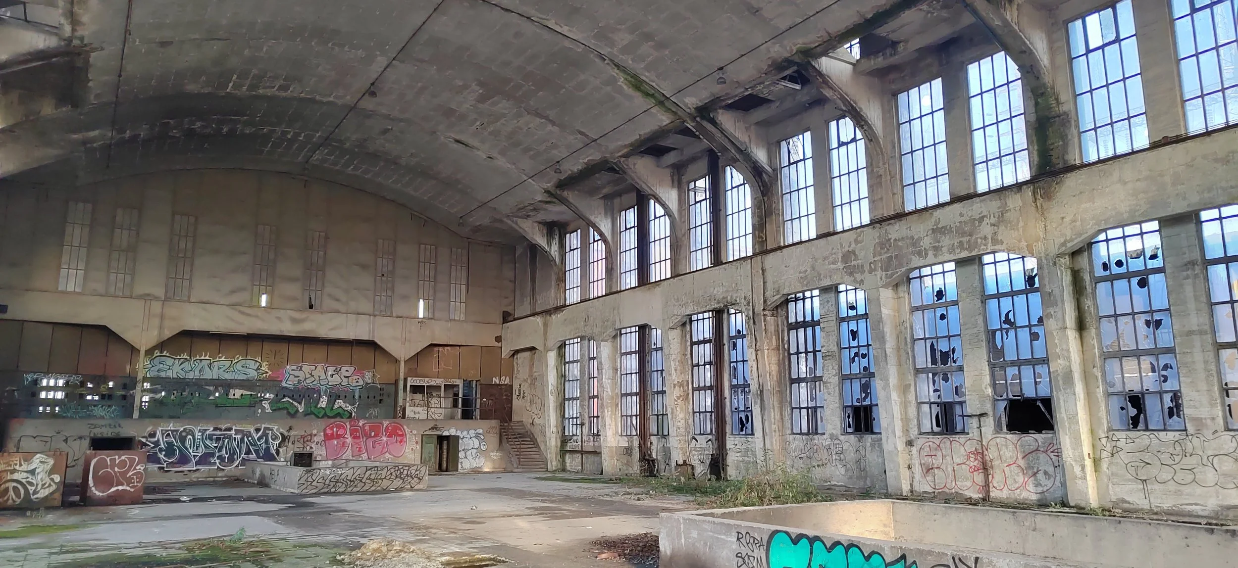 Verfallenes, verlassenes Gebäude mit großen, verzierten Fenstern, die teilweise zerbrochen sind, und Graffiti an den Wänden.