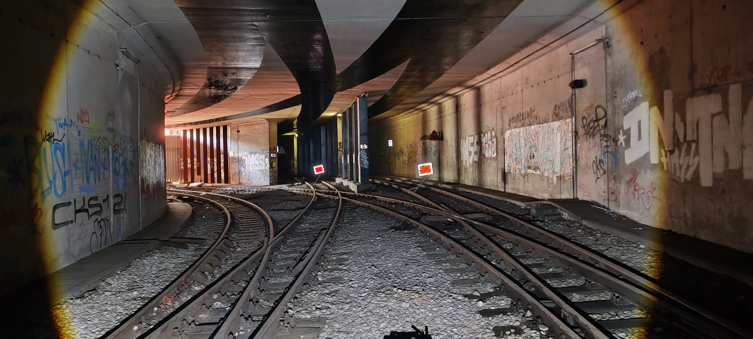 Bahnstrecke führt durch einen Tunnel mit Graffiti an den Wänden, die an den Seiten beleuchtet sind.
