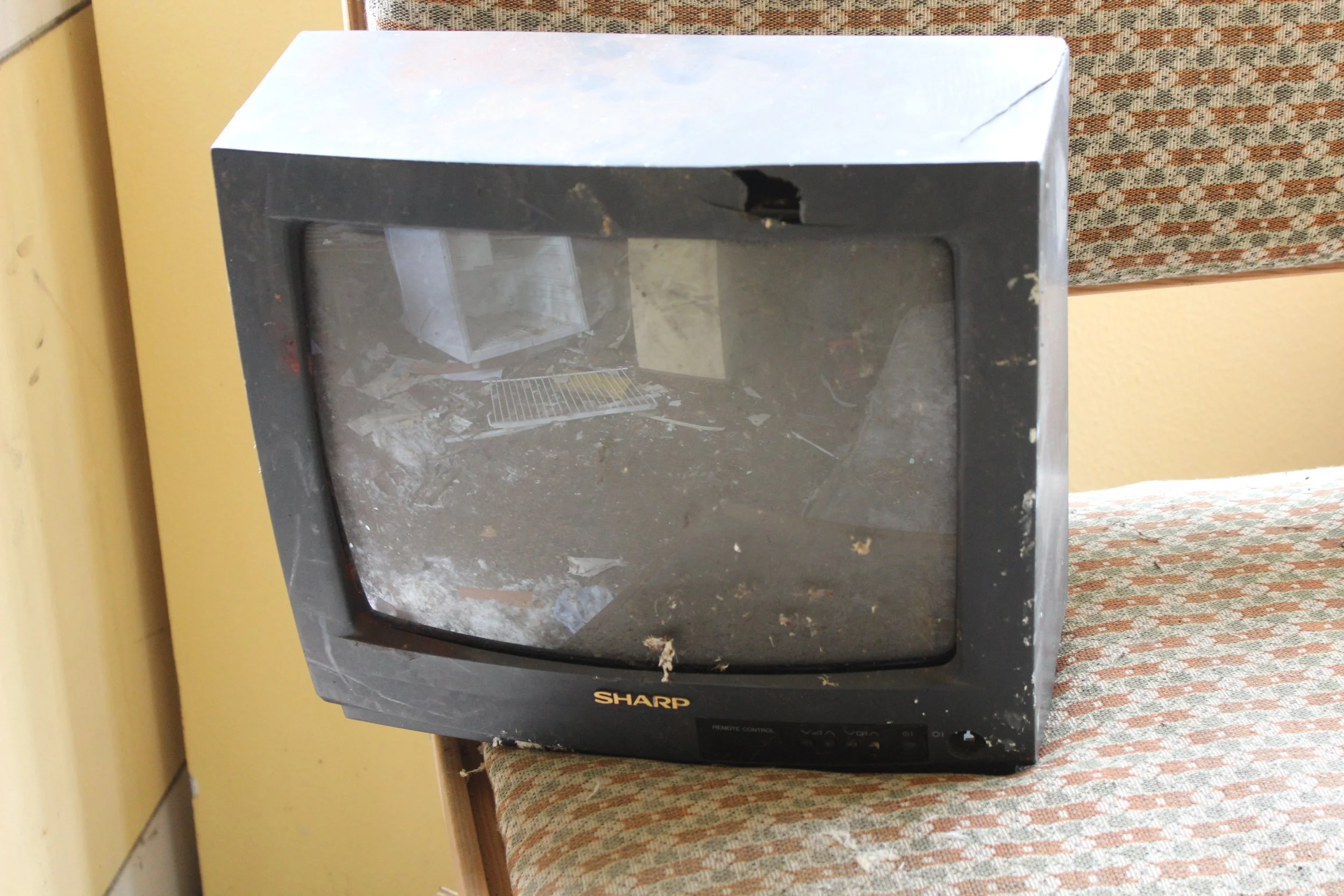 Ein alter, staubiger Fernseher der Marke Sharp auf einem Sitzkissen