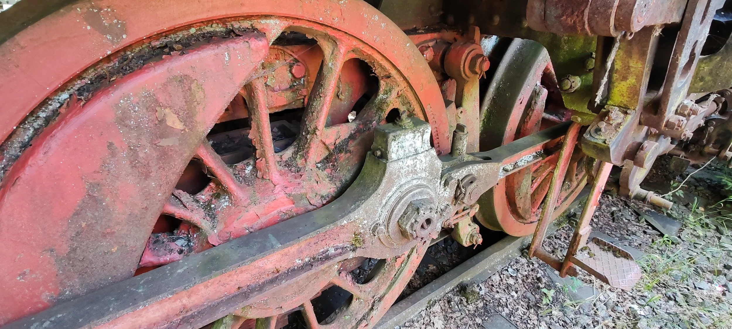 Alte, rostige Dampflokomotive mit großen Radsätzen und Antriebsmechanismus, die im Freien steht, umgeben von Natur, Staub und Moos.