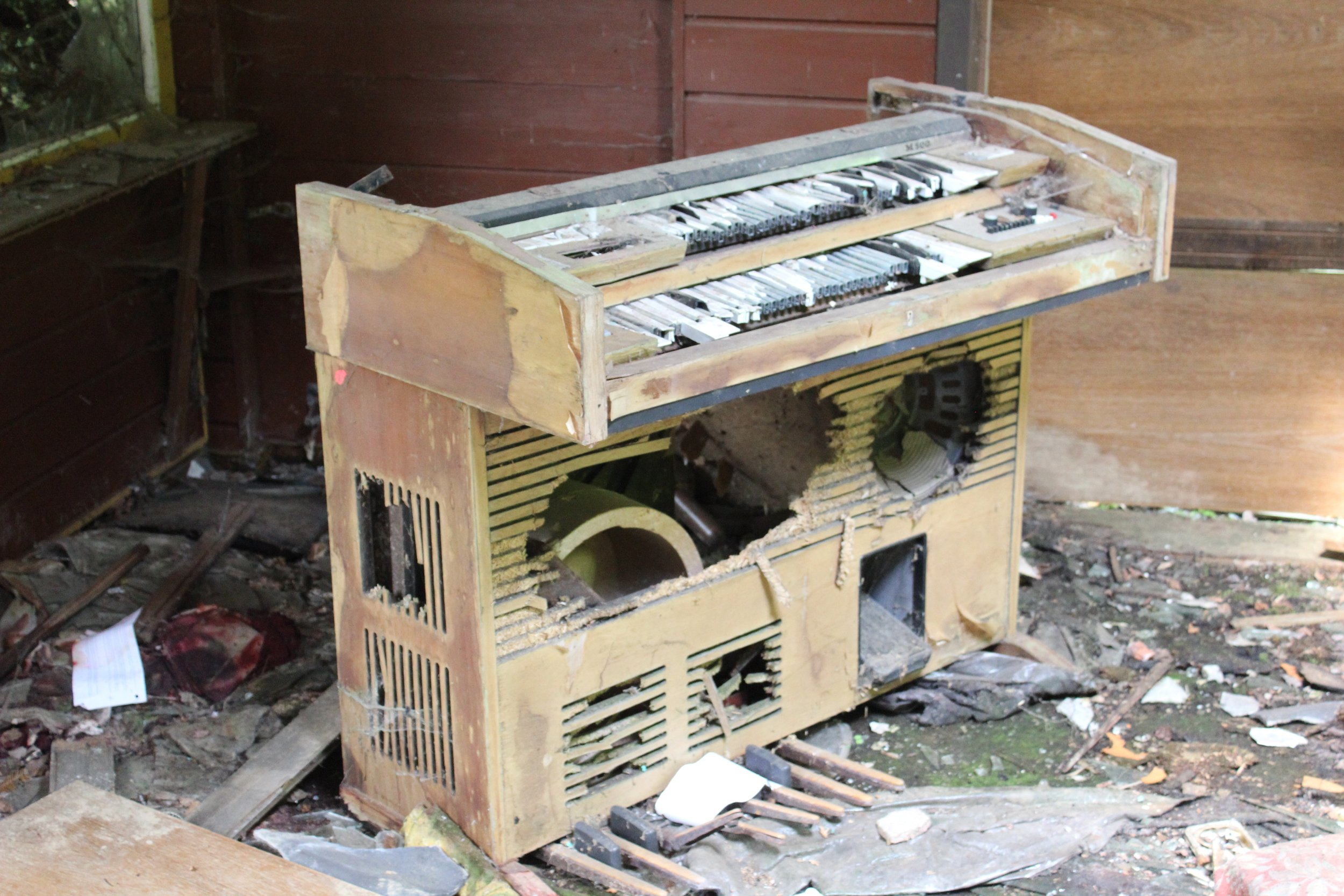 Verlassenes, kaputtes Klavier in einem verfallenen Raum, umgeben von Müll und Schmutz.