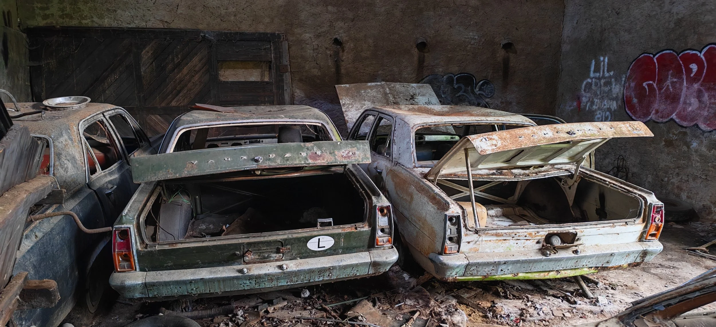 Verlassene, verrostete Autos in einer dunklen Garage oder einem Schuppen mit Graffiti an der Wand.