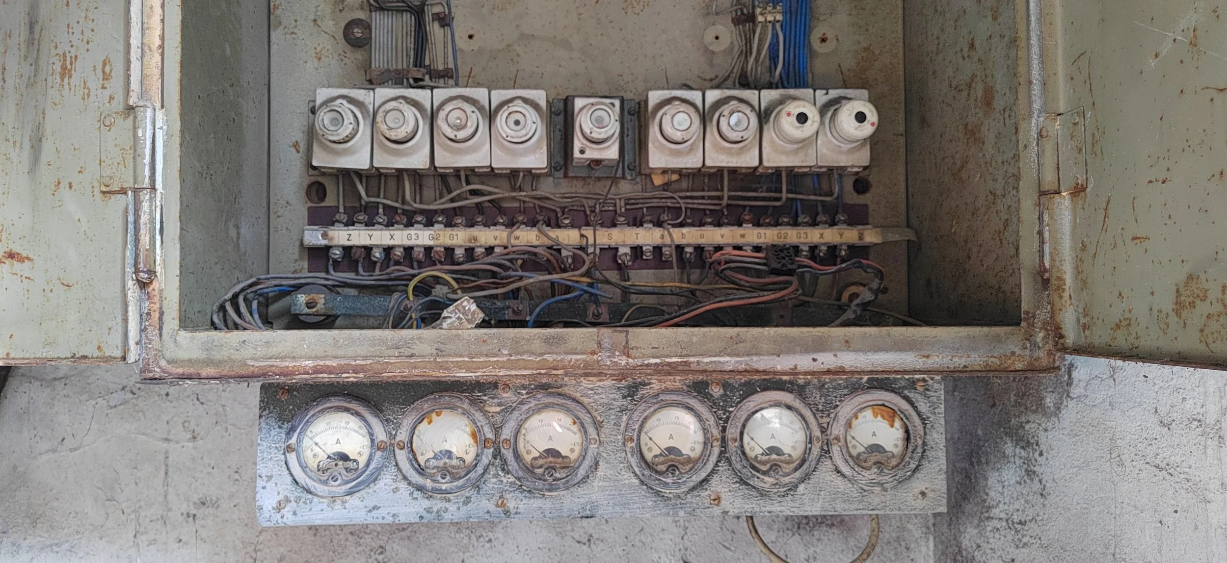 Altes, offenes elektrisches Steuergerät mit mehreren Sicherungen, Kabeln und Messgeräten, die verschmutzt und rostig sind.