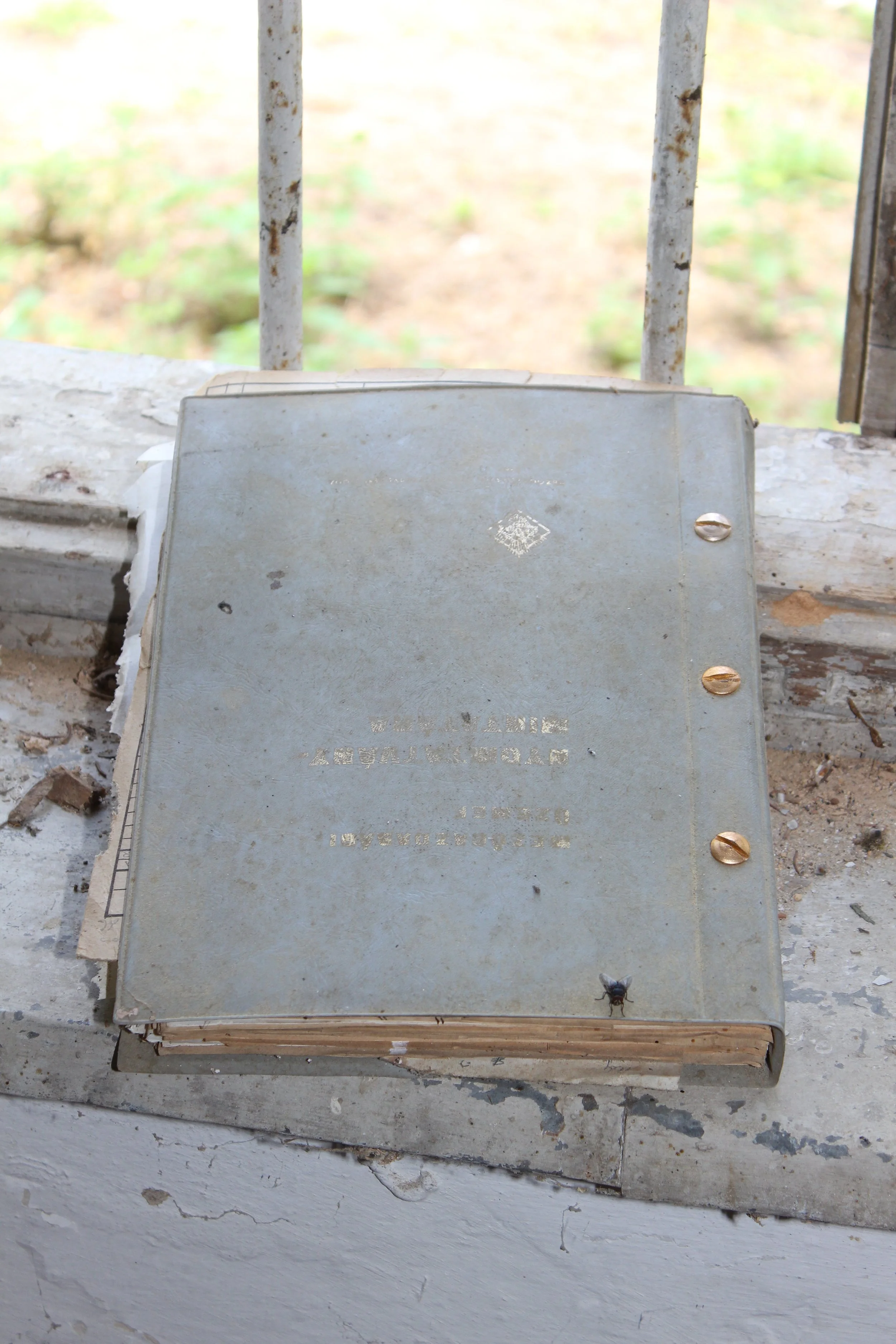 Ein verstaubtes, altes Buch liegt auf einer staubigen Fensterbank, die durch Gitterstäbe geschützt ist.