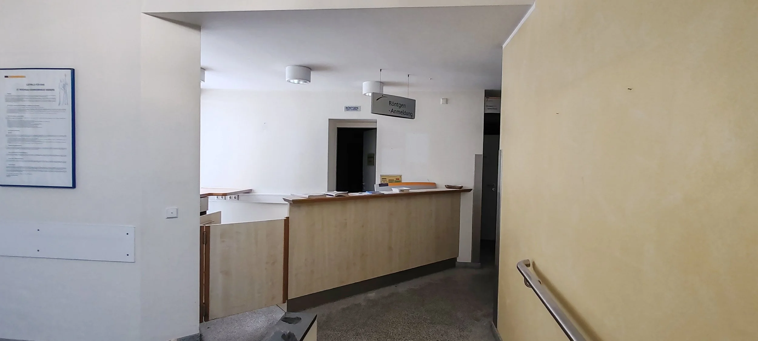 Innenaufnahme eines medizinischen Rezeptionstresens im Gesundheitszentrum, mit Hinweisschildern und einem Handlauf an der Wand.