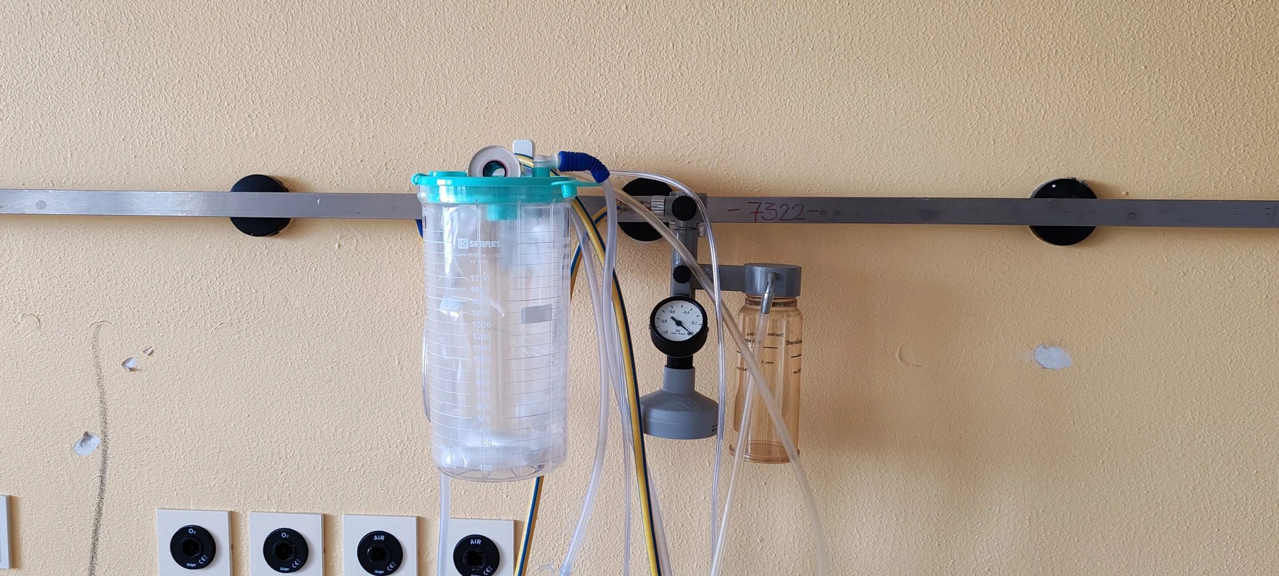 Medizinische Geräte und Schläuche an einer gelben Wand, darunter Steckdosen und Regler.