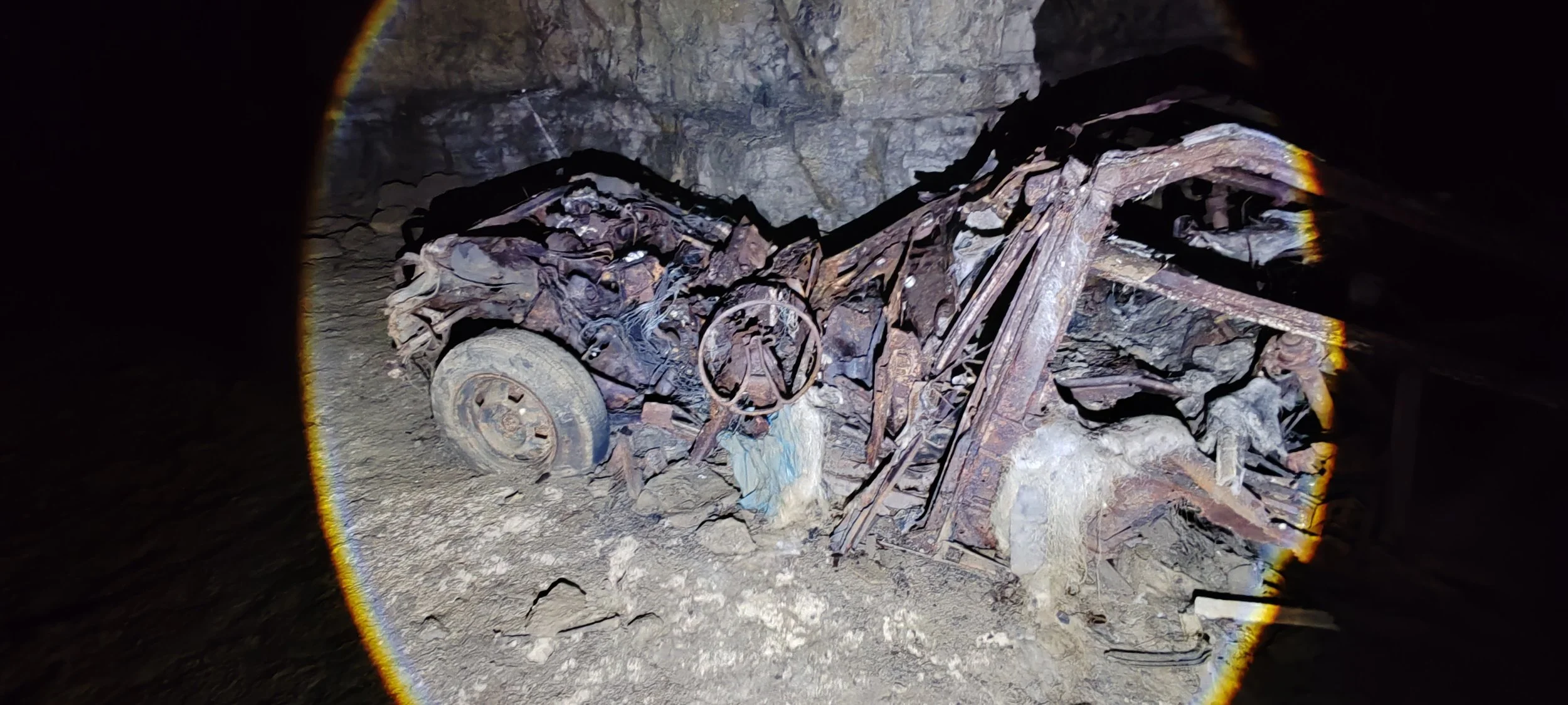 Verrostete Fahrzeugreste in einer Höhle, aufgenommen mit Taschenlampe