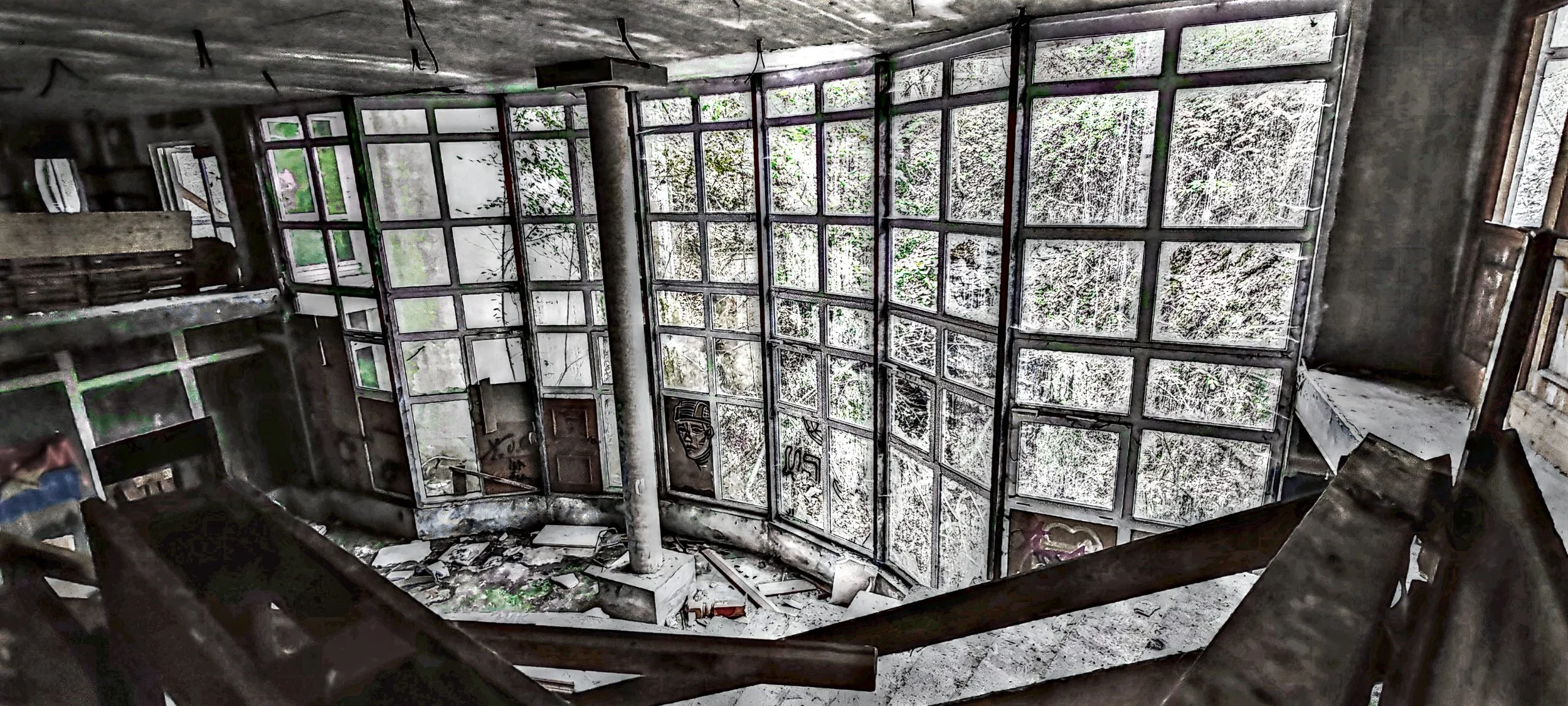 Verfallene, verlassene Inneneinrichtung mit zerbrochenen Fenstern und Graffiti an den Wänden.