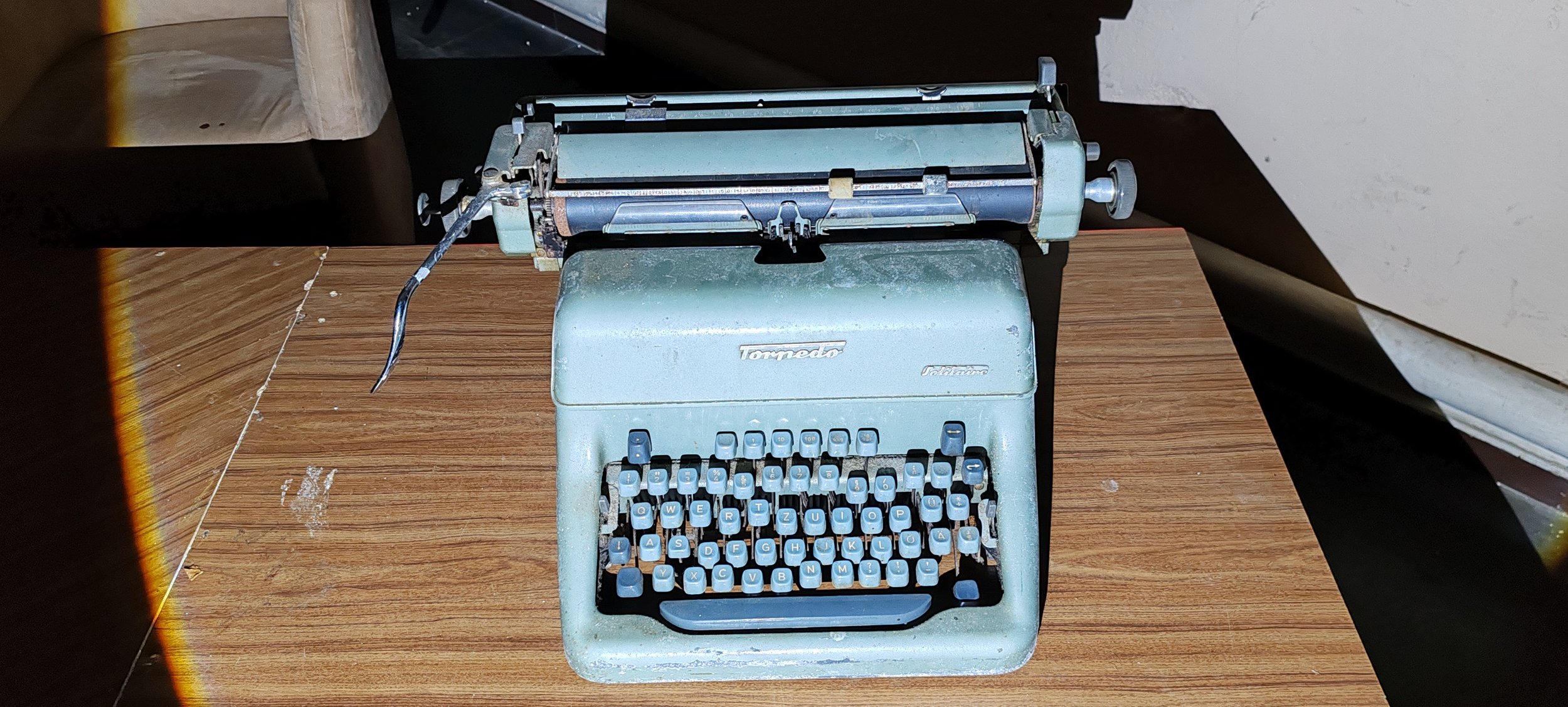 Alte grüne Schreibmaschine auf einem Holztisch, mit sichtbarem Tasten und Papierrollenhalter.