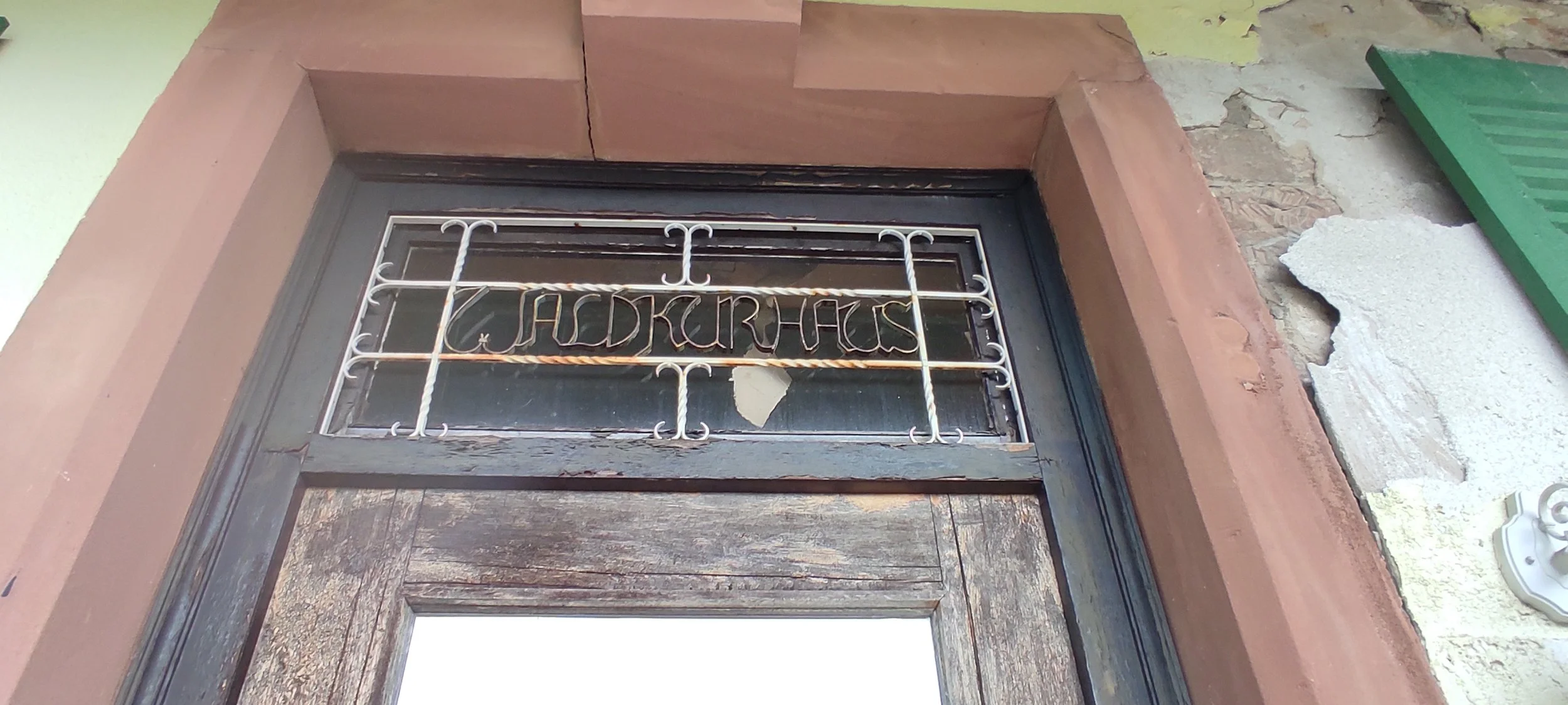 Ein Fenster mit einem Gitter aus weißen Eisenstangen, auf dem das Wort „JADKURHAUS“ geschrieben steht.