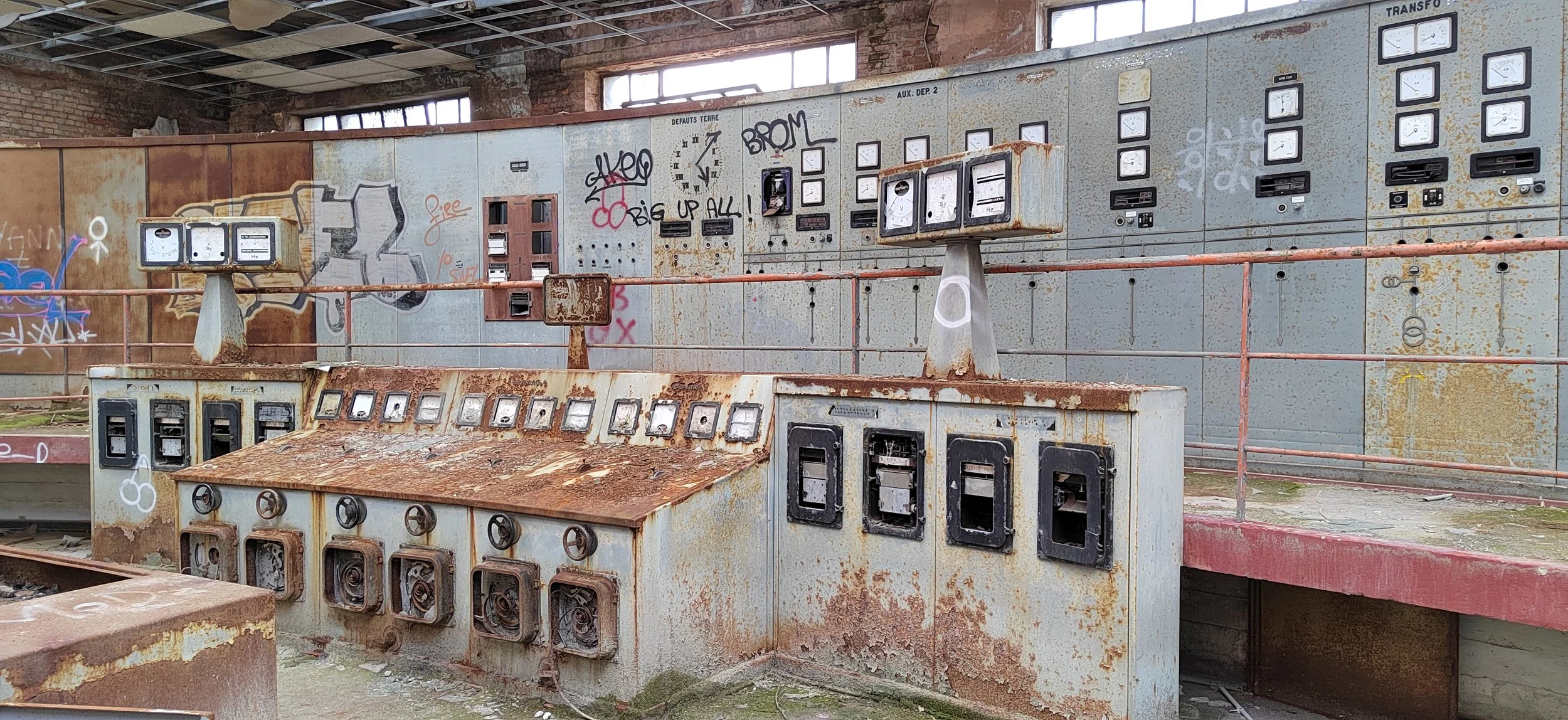 Veraltete, rostige elektrische Schaltanlagen und Zähler in einem verlassenen Gebäude mit Graffiti und zerbrochenen Fenstern.