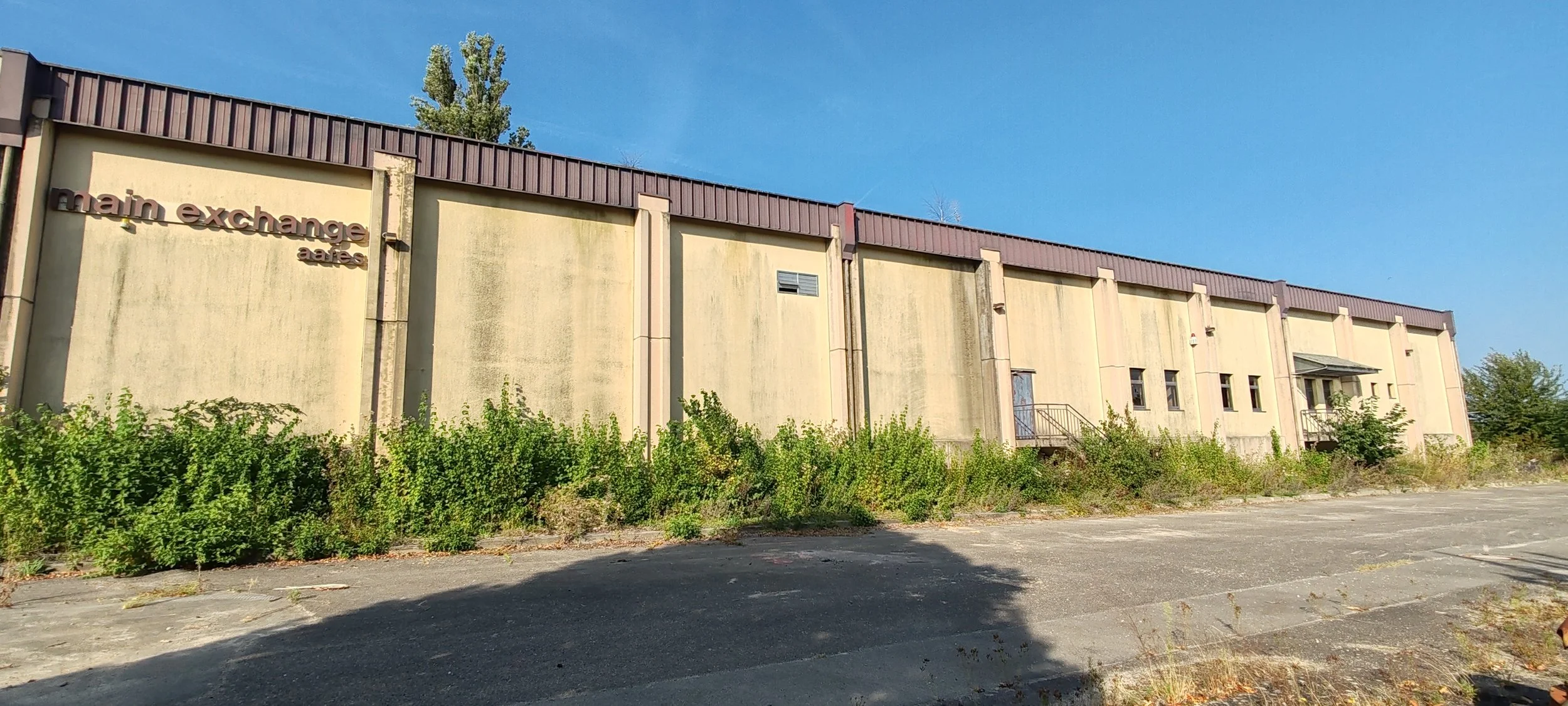 Verfallenes Gebäude mit einem verfallenden Parkplatz im Vordergrund und einem blauen Himmel im Hintergrund.