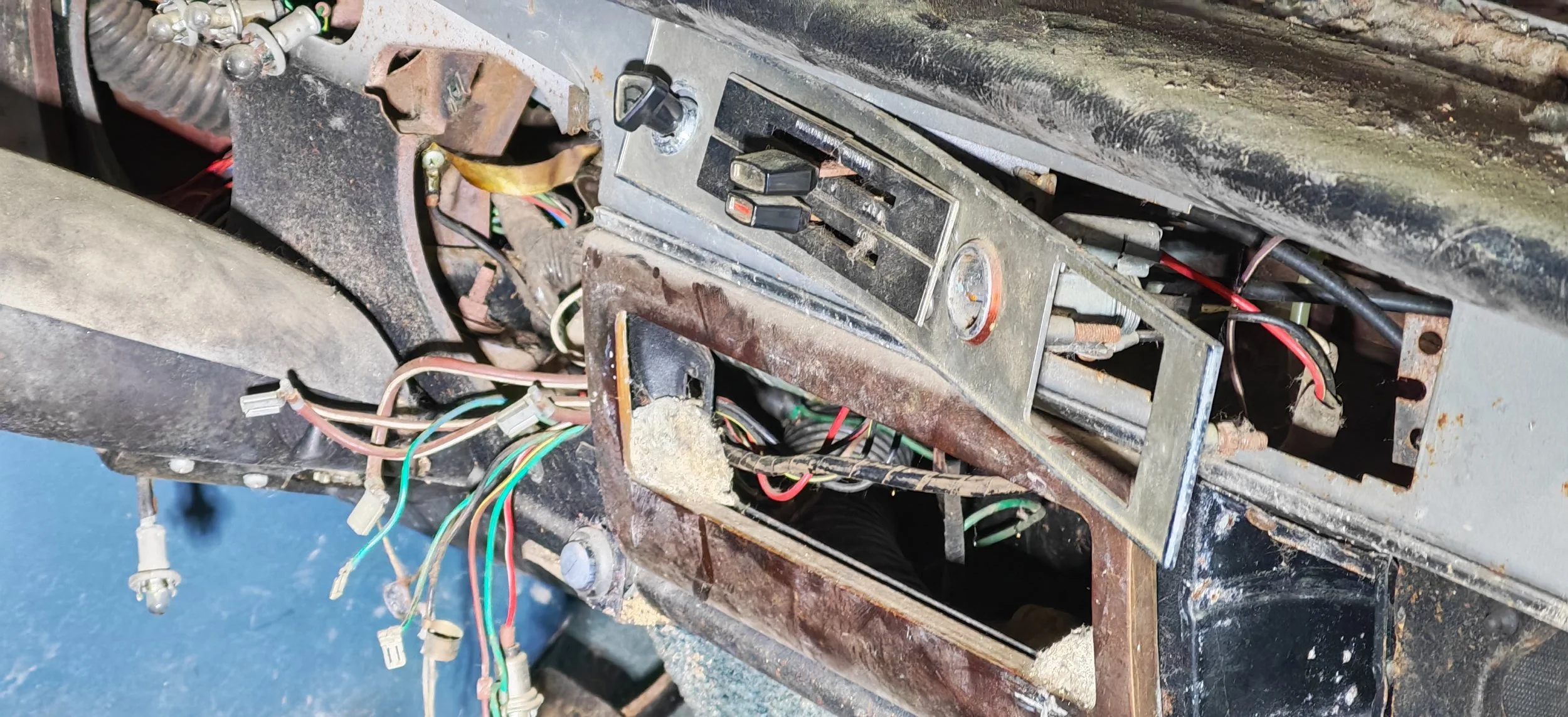 Alte, rostige Autoblende mit offenem Armaturenbrett, sichtbare Kabel und elektrische Komponenten.