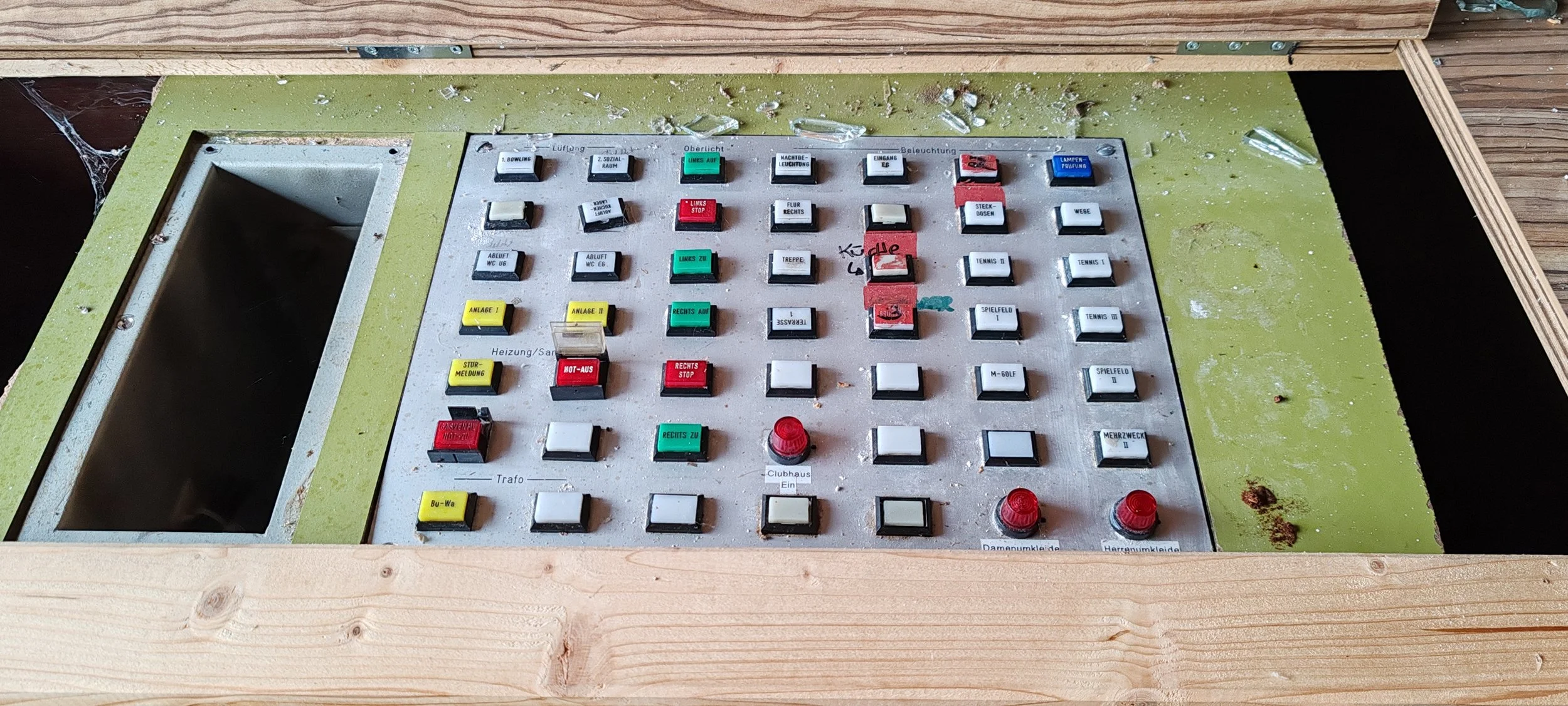 Alteres Steuerpult oder Schalttafel mit zahlreichen Tasten, Reglern und Kabeln, teilweise mit Beschriftungen in Deutsch, auf einem Holzrahmen.