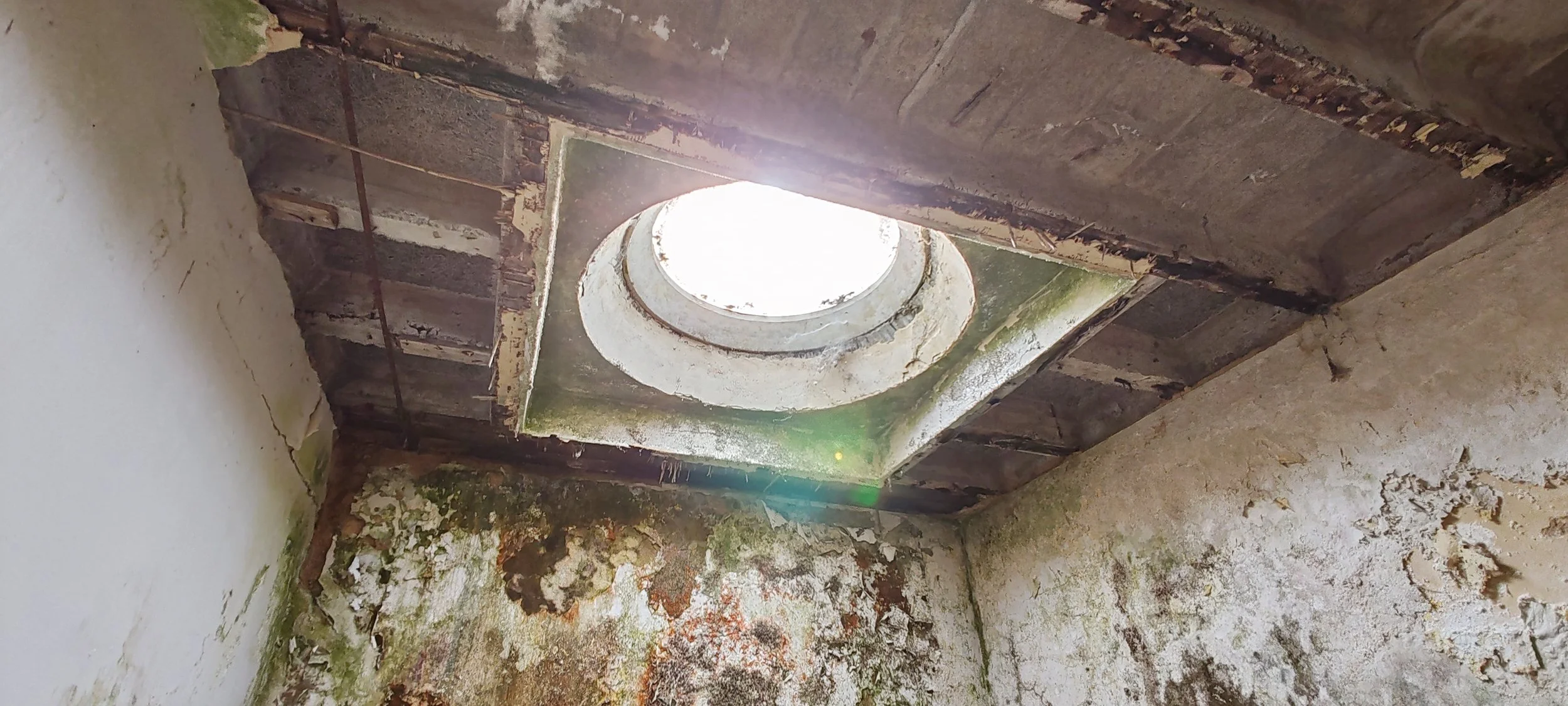 Ein Blick nach oben durch ein runden Loch in der Decke eines alten, verfallenen Raumes mit schimmeligen, beschädigten Wänden.
