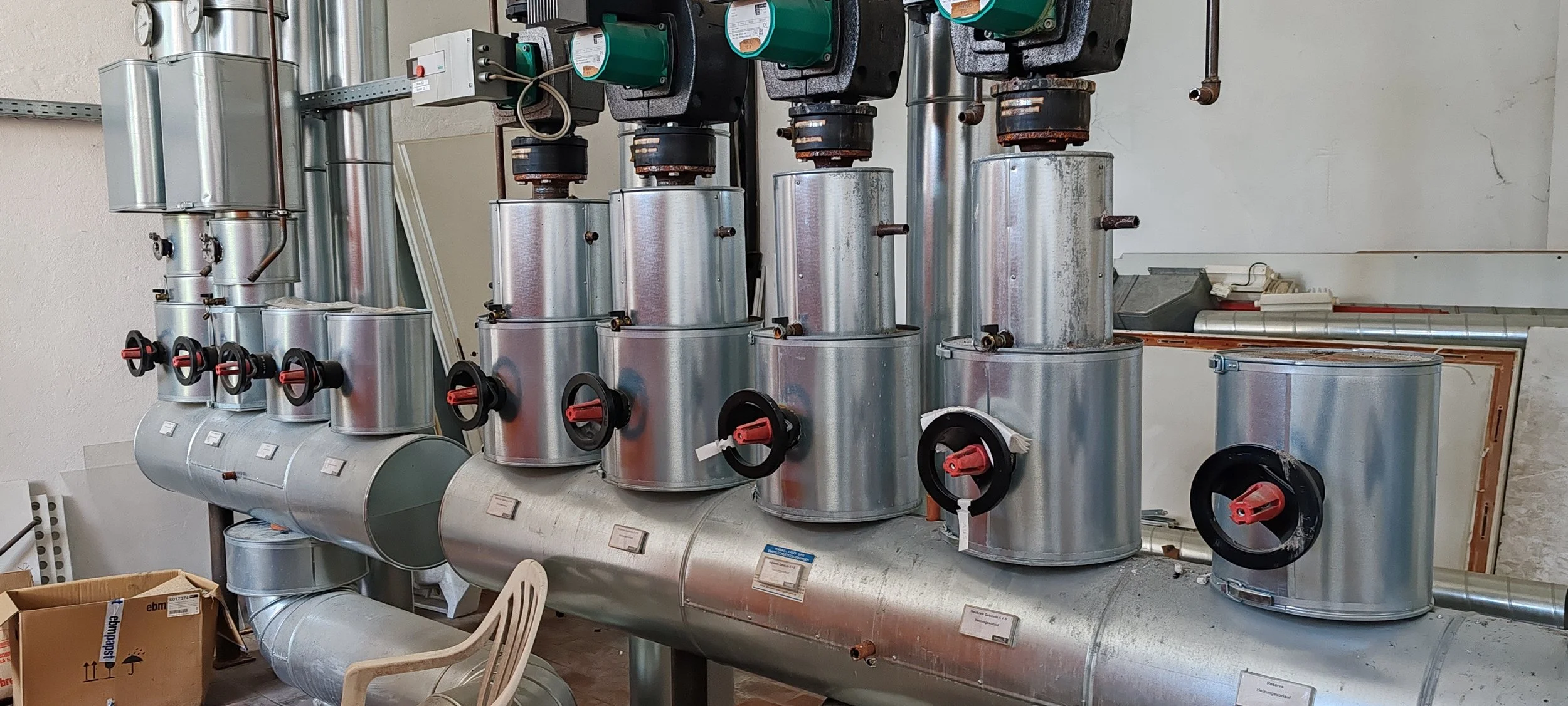 Industrielle Heizungs- oder Klimaanlagen mit Rohren, Ventilen und Steuerungen in einem Technikraum.