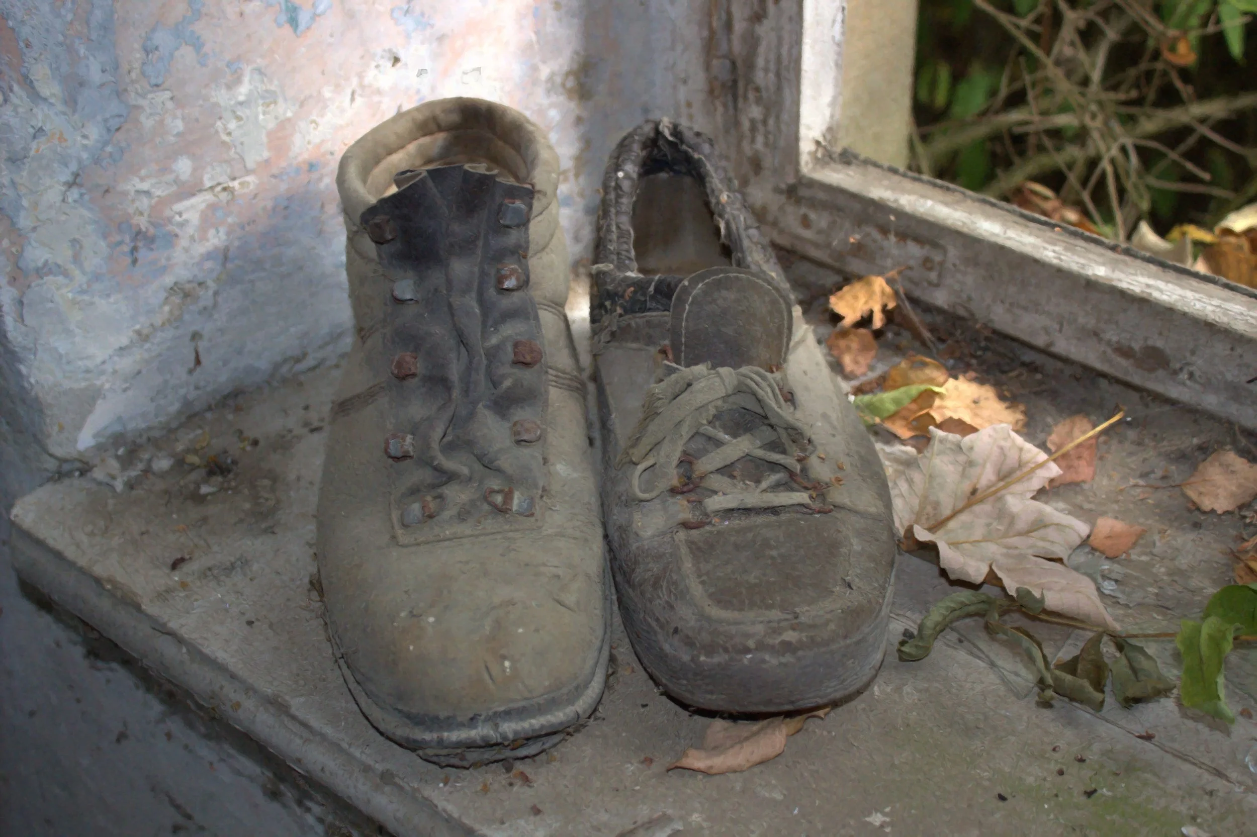 Alte, abgenutzte Turnschuhe, die neben einem Fenster mit Herbstlaub liegen.