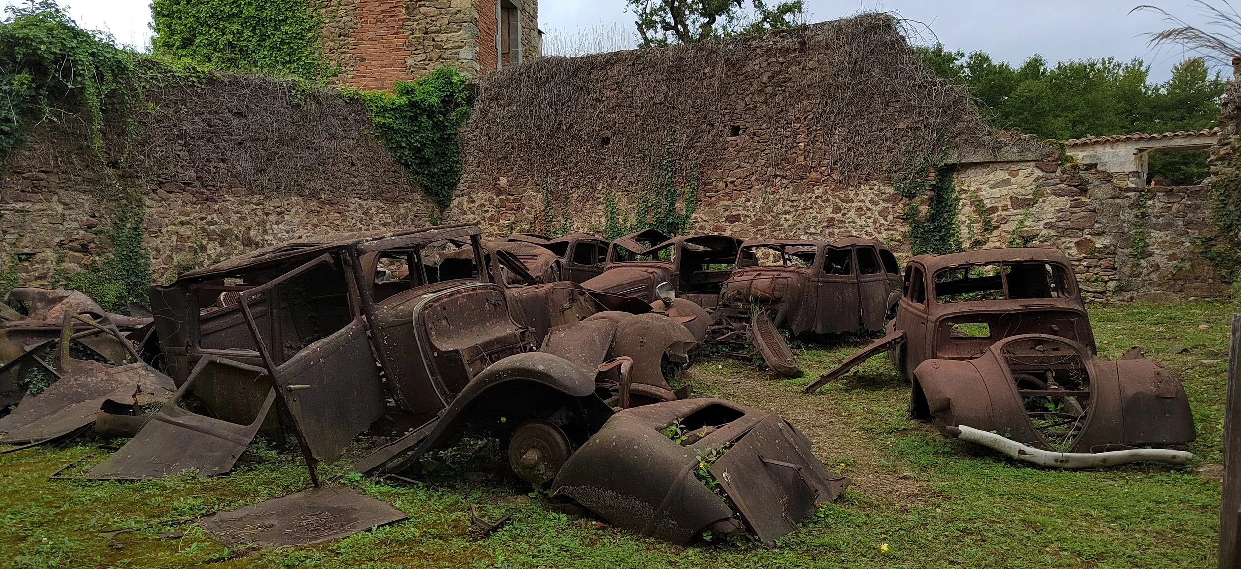 Verrostete alte Autos vor einer alten Steinmauer, umgeben von Vegetation.
