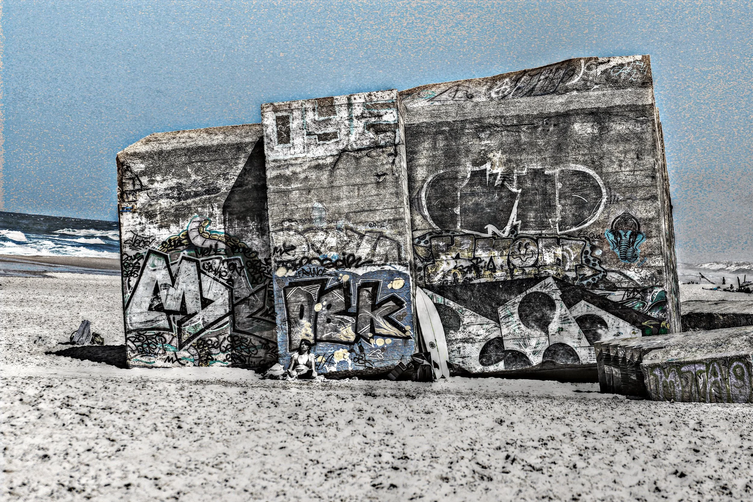 Graffiti bedecktes Betongebäude am Strand mit Meereswellen im Hintergrund.