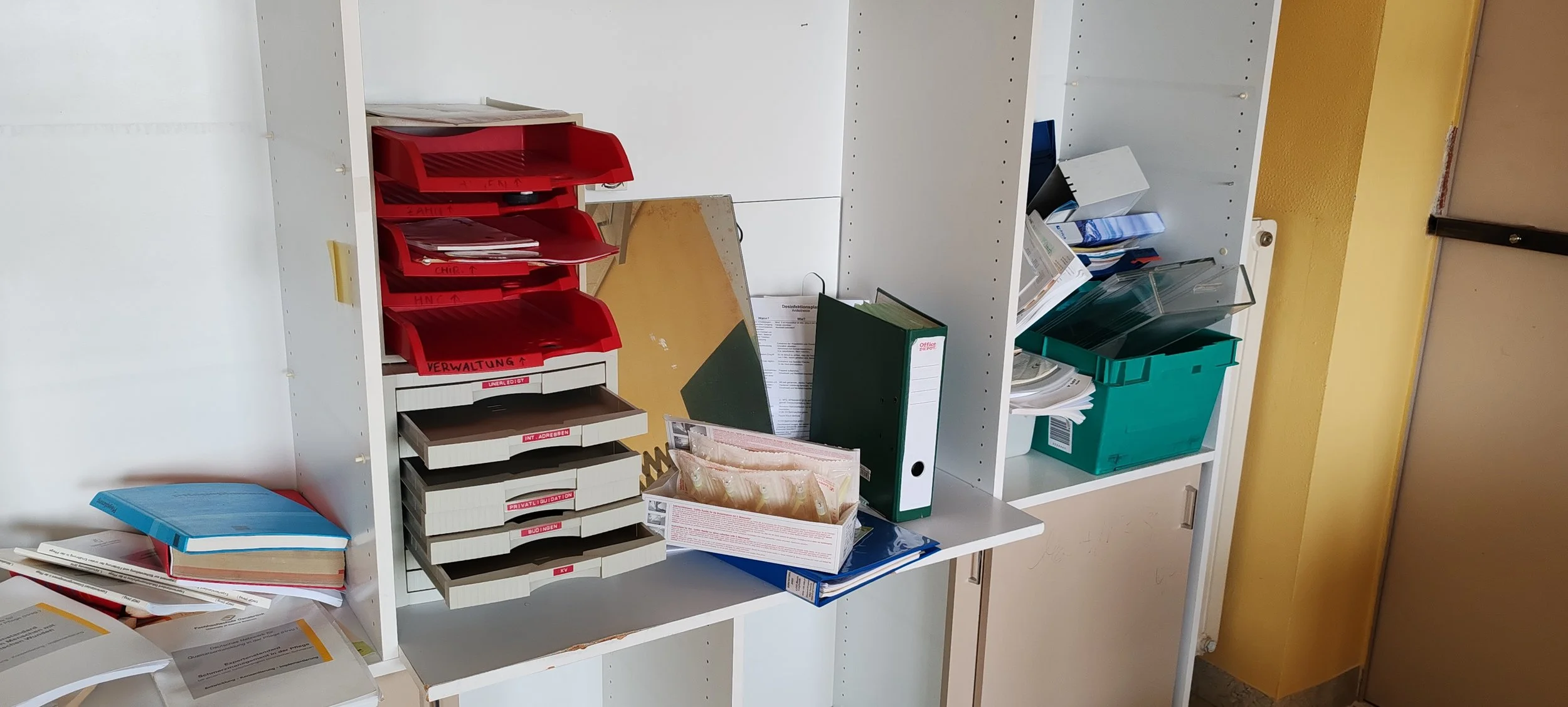 Büroregale mit Akten, Ordnern und Büromaterialien, unordentlich, auf einem schwarzen Tisch.