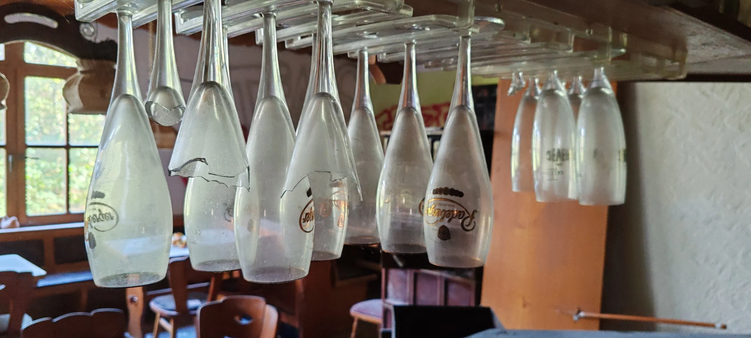 Hängende Weingläser in einer rustikalen Gaststube mit Fenster im Hintergrund.