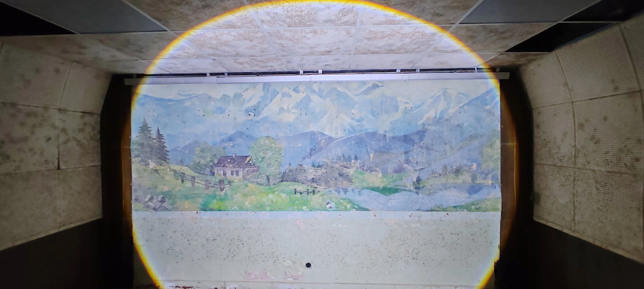 Fotografie eines beleuchteten Gemäldes eines Bergdorfes mit Bergen im Hintergrund, eingerahmt von einem Tunnel mit Steinwänden, durch den die Szene sichtbar ist.