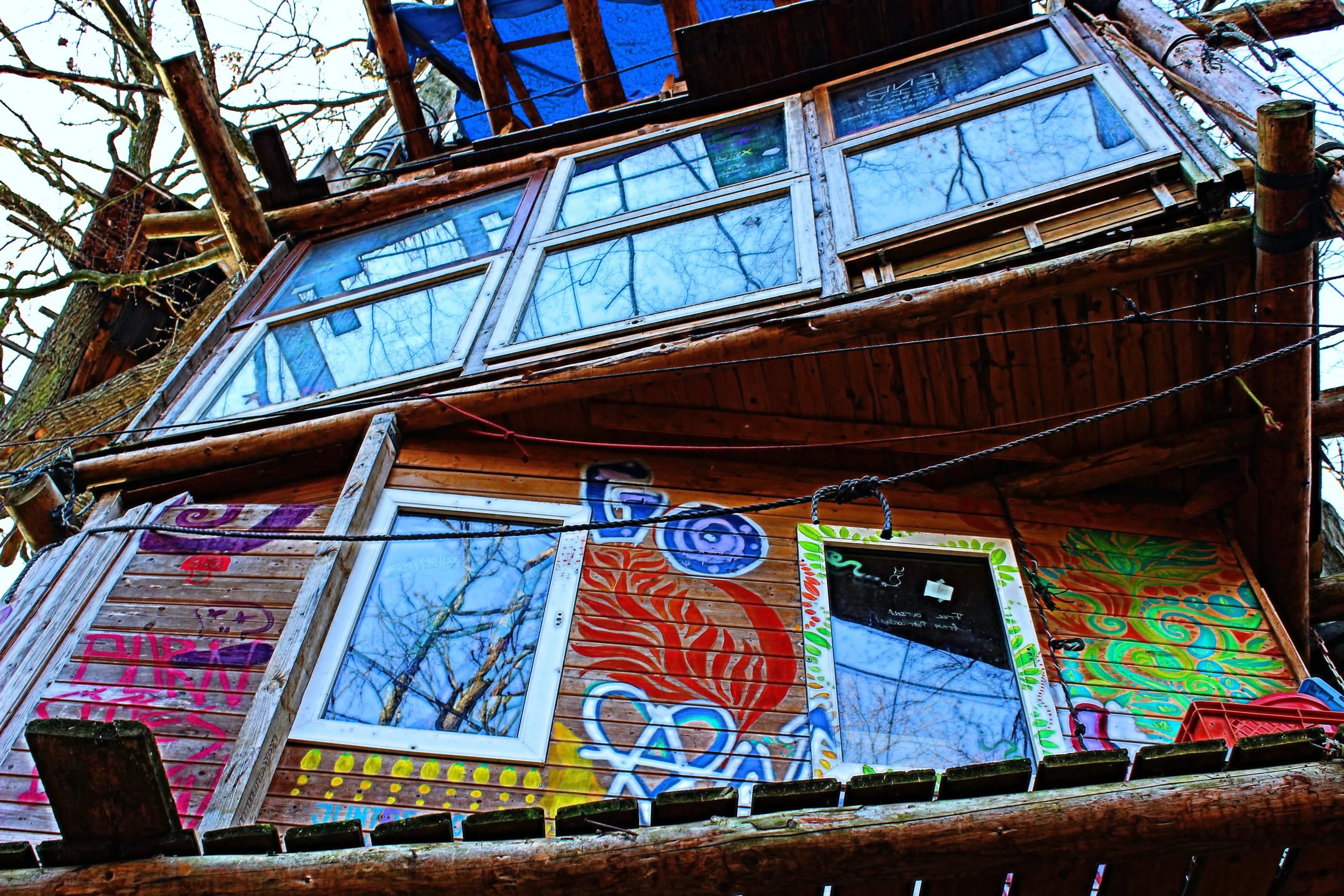 Bunte bemalte Baumhaushütte mit großen Fenstern, bemalt mit Schweif- und Spiralmustern, in den Ästen eines Baumes.