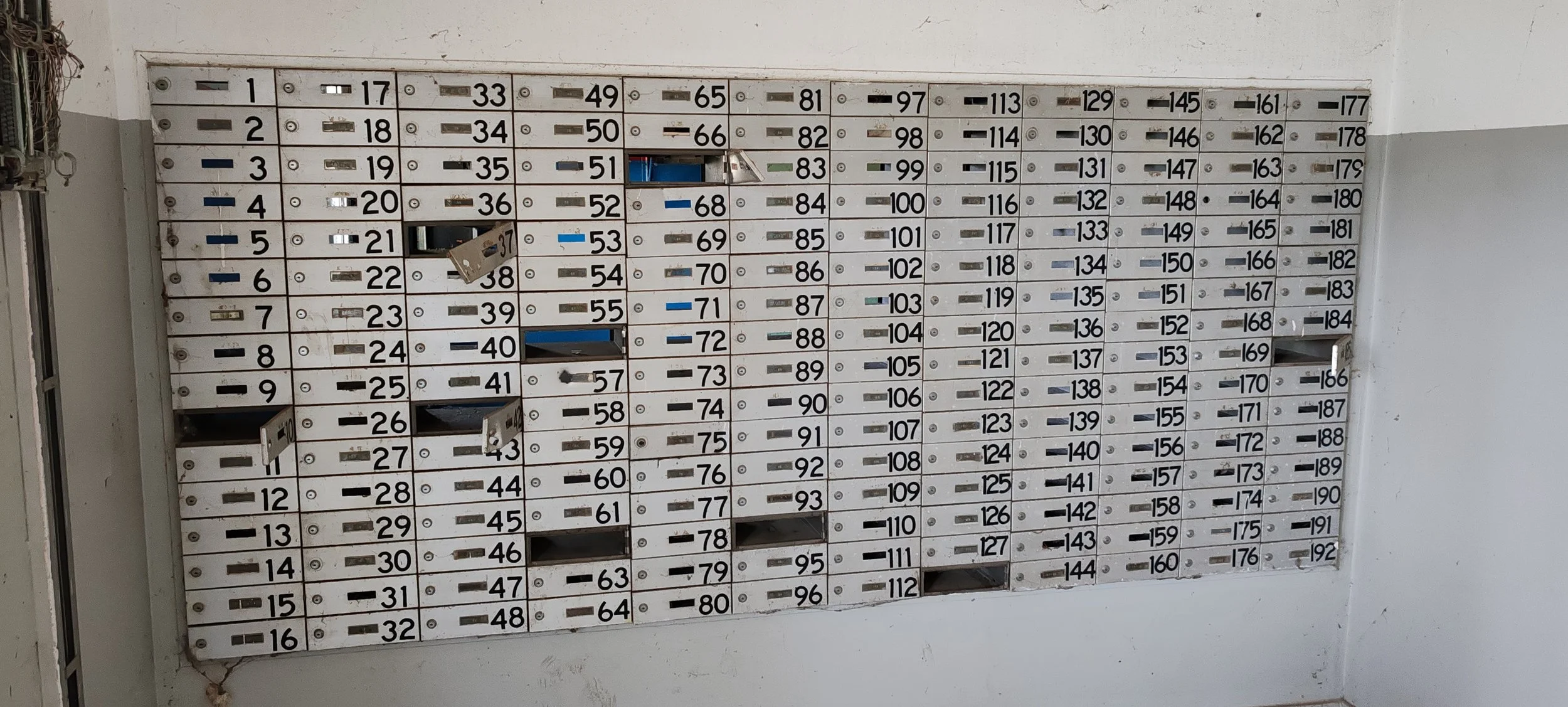 Mehrfamilienhaus-Briefkästen mit nummerierten Fächern, einige Fächer sind offen, in einer befindet sich eine Postsendung.