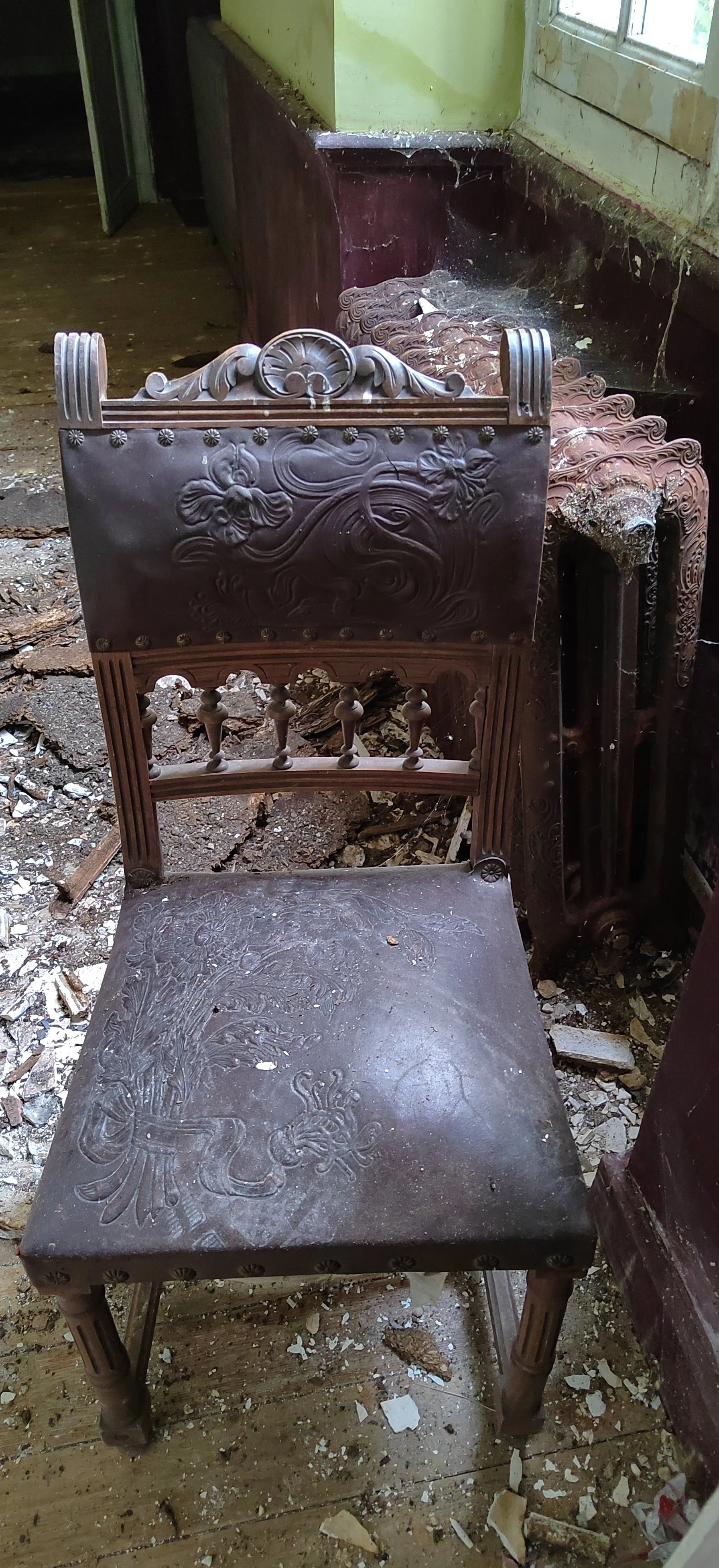 Ein antiker, kunstvoll geschnitzter Holzstuhl in einem alten, verfallenen Raum mit Schmutz und Trümmern auf dem Boden.