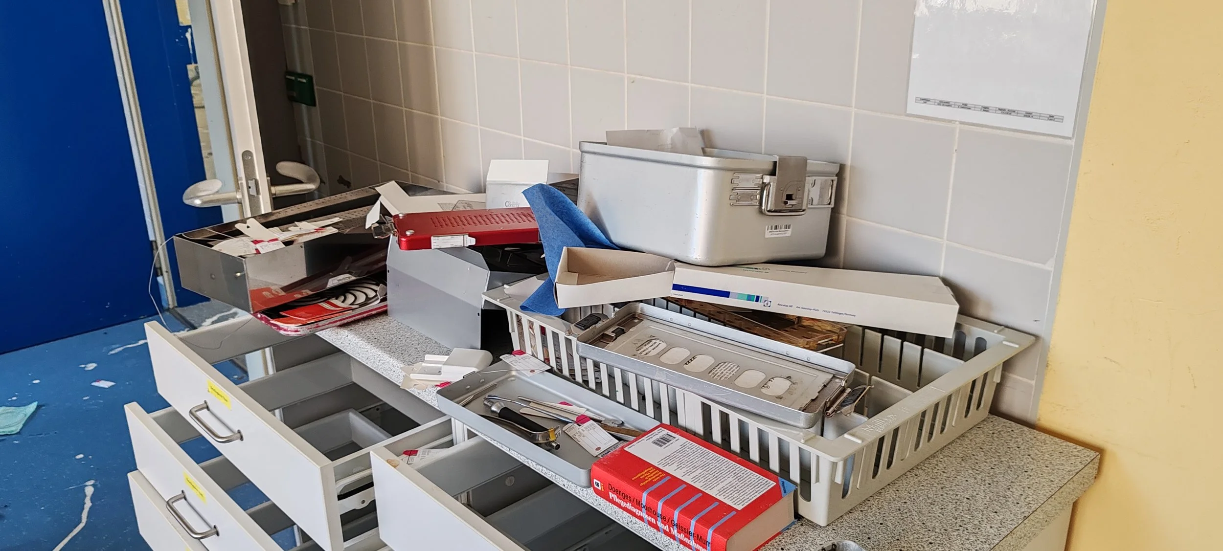 Un zerbrochenes und unordentliches Arzneimittelregal oder -schrank mit verschiedenen medizinischen Gegenständen, Papieren und Behältern auf einer weißen Arbeitsplatte.