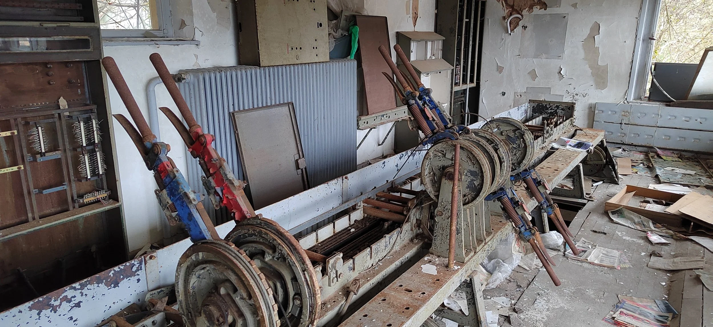 Ein verrosteter, alter Aufzugskasten in einem verlassenen, ramponierten Raum mit zerbrochenen Fenstern und verstreutem Schutt auf dem Boden.