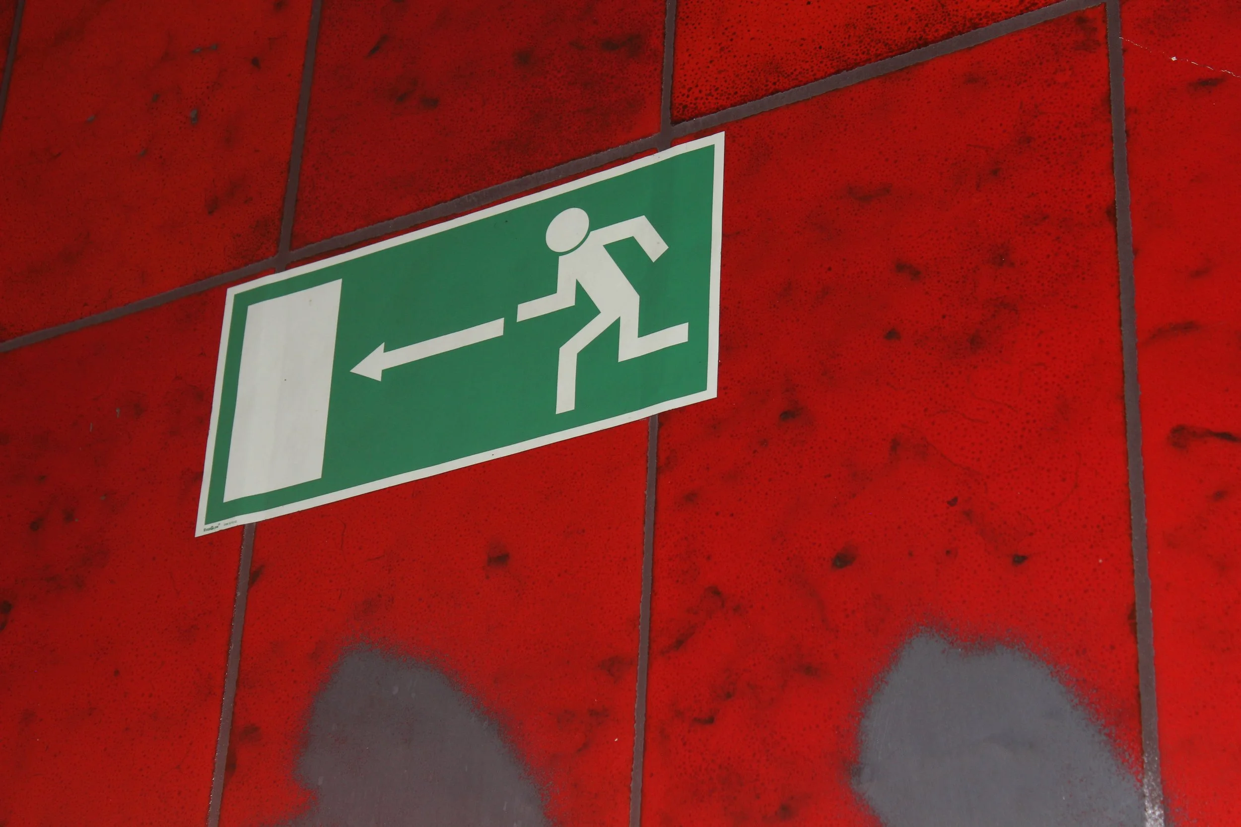 Grüner Rettungsweg-Aushang an roter Wand, zeigt mit Pfeil nach links.