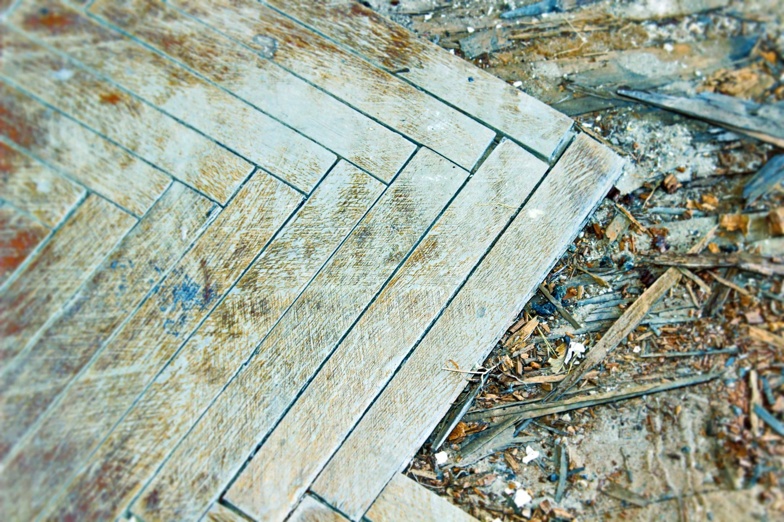 Verwitterte Holzplanken neben Schutt und Sand auf dem Boden.