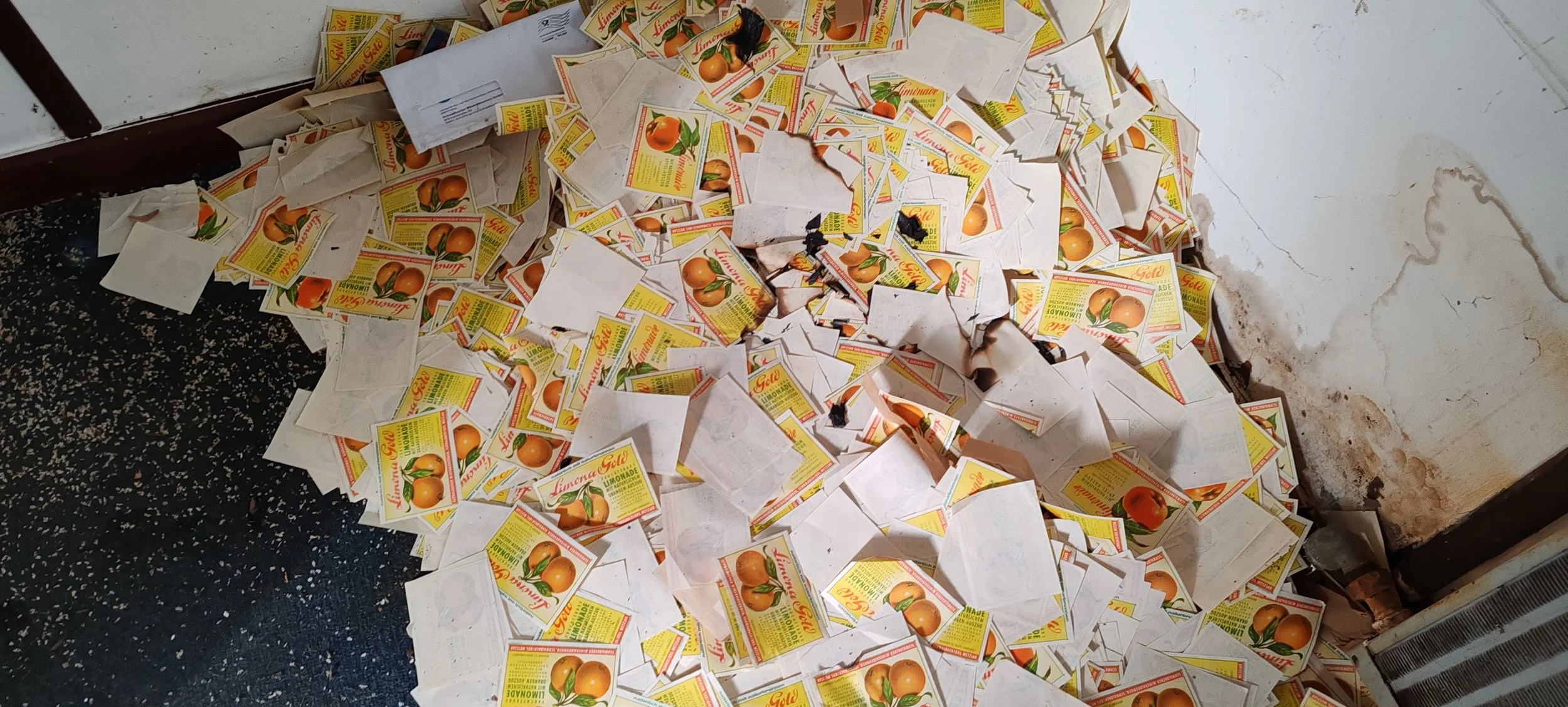 Viel zerknüllte und verstreute Verpackungen von Limona Gold Limonade auf einem Boden in einem Raum.