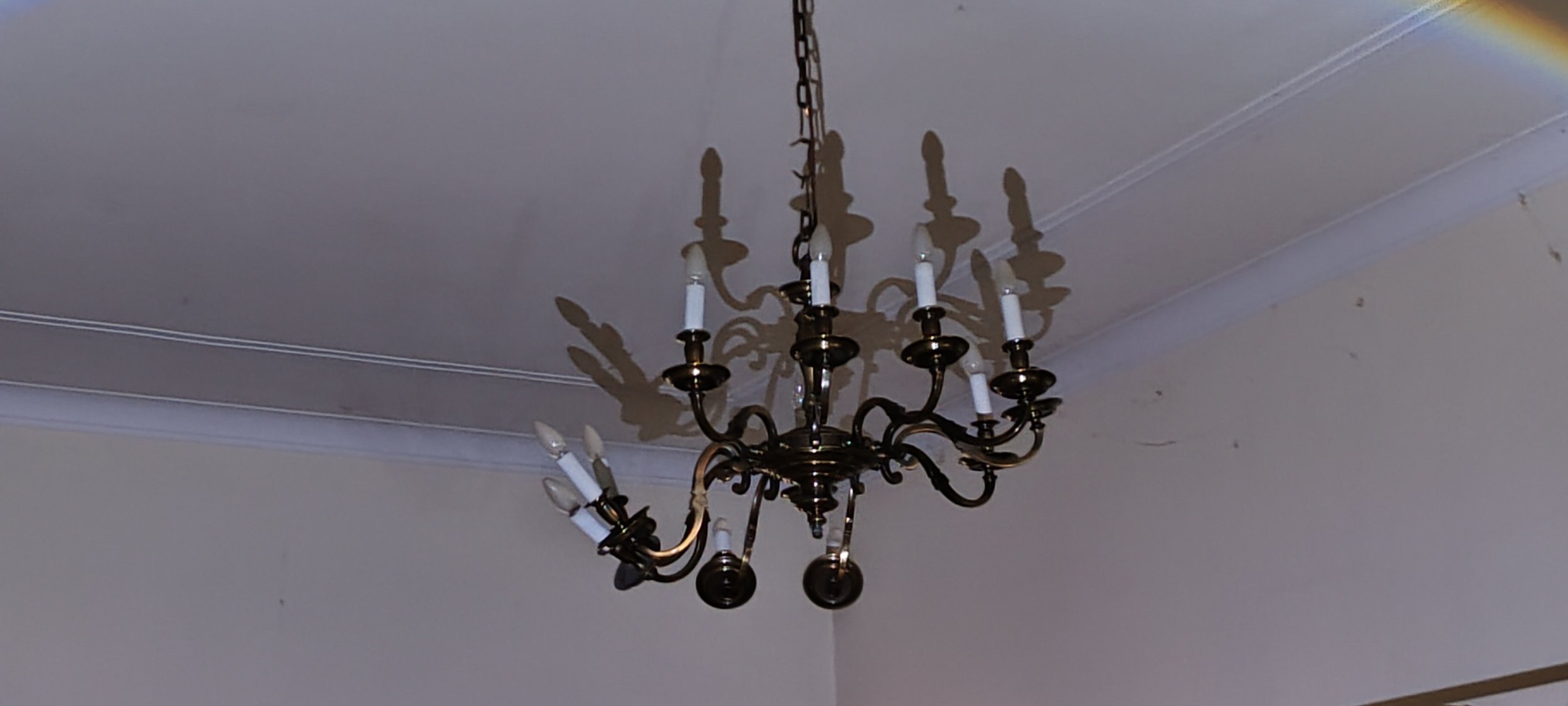 Ein alter Kronleuchter mit mehreren Kerzenhaltern hängt an der Decke eines Raums.