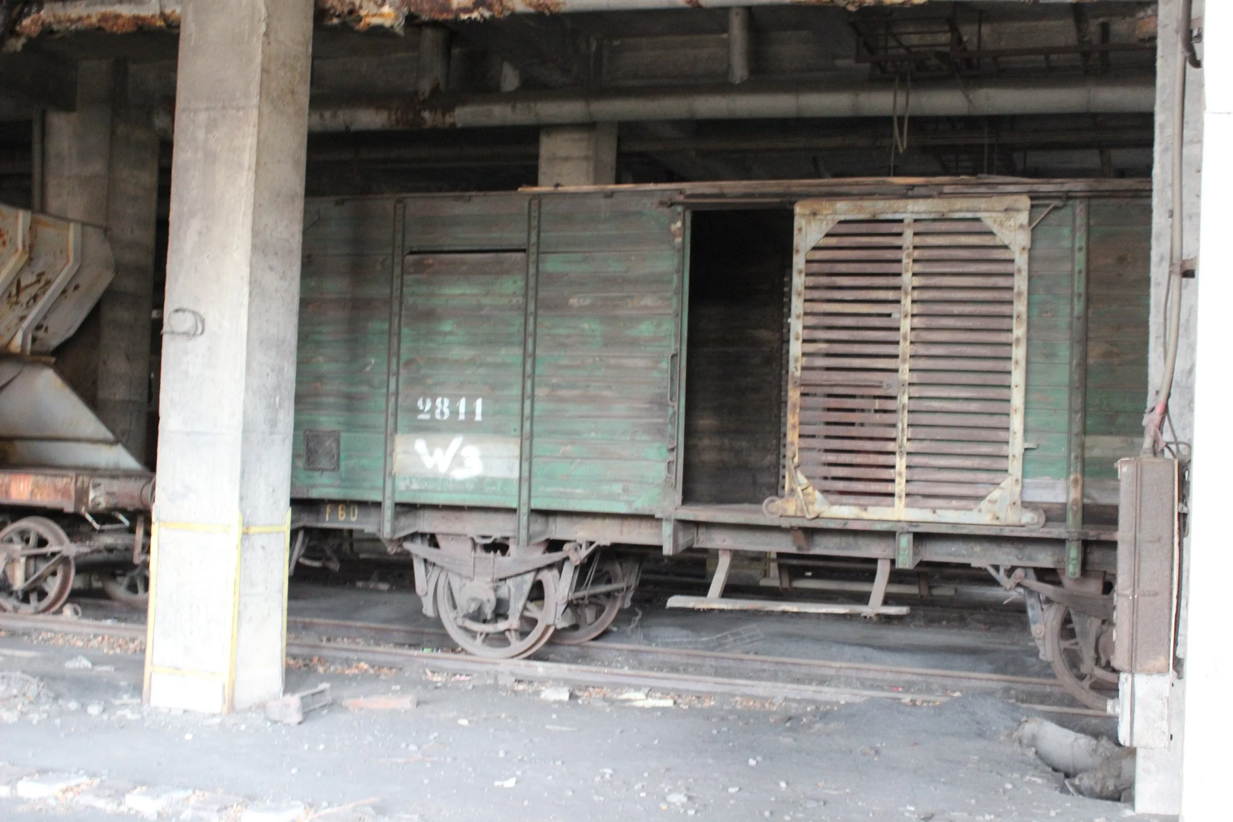 Alte, grüne Eisenbahnwagons in einem Bahnhof oder Lagerhalle, der Wagon auf der Seite sichtbar mit Öffnung und Fahrzeugrädern