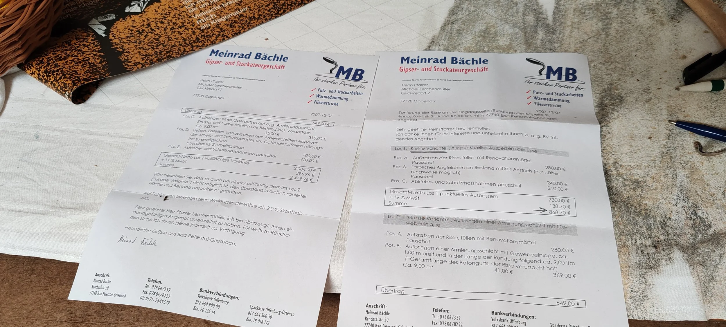 Zwei Rechnungen von Meinrad Bächle, Gipser- und Stuckateurgeschäft, liegen auf einem Tisch. Die Rechnungen sind in Deutsch geschrieben und enthalten Details zu Arbeiten und Preisen. Es befinden sich einige Schreibutensilien und andere Gegenstände um 