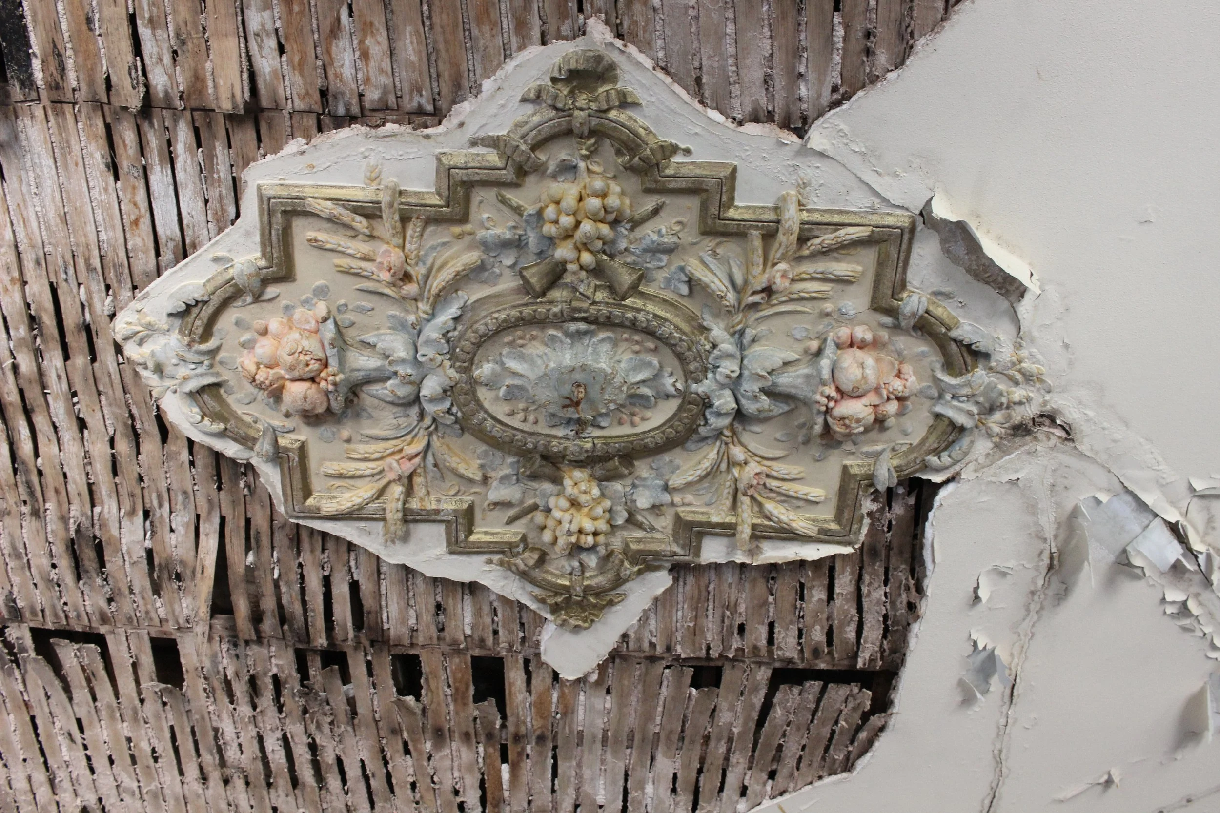Verzerrtes, antikes geschnitztes Deckenmedaillon in einem alten Raum mit beschädigter Deckenverkleidung und Rissen in der Decke.