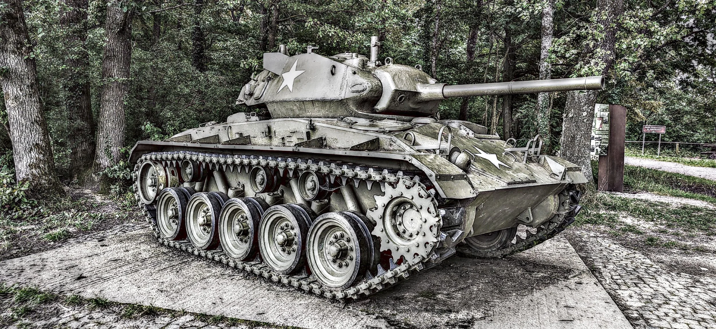 Ein alter Military-Panzer steht im Wald auf einem Steinboden.