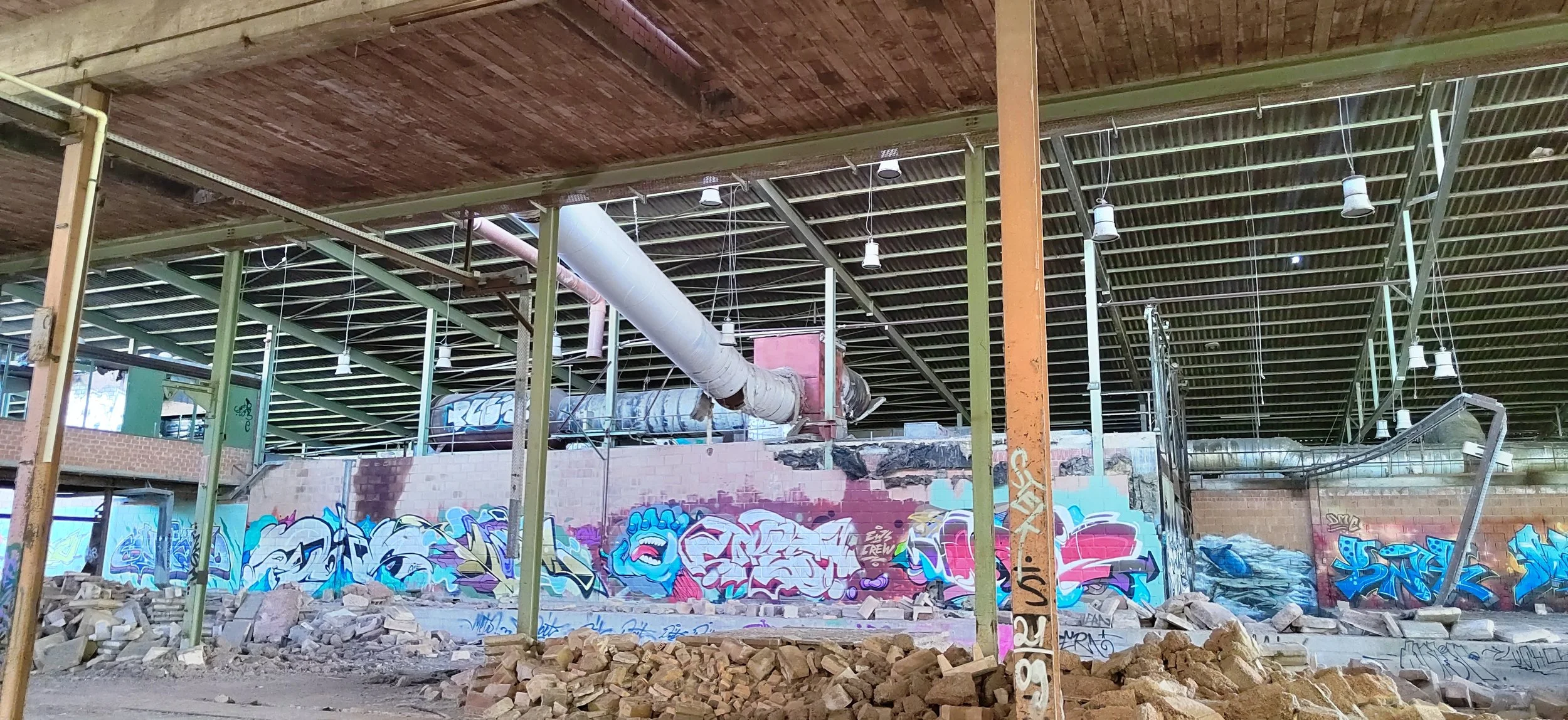 Innenansicht eines verlassenen Gebäudes mit Graffiti auf den Wänden, herumliegenden Steinen und zerbrochenem Boden.